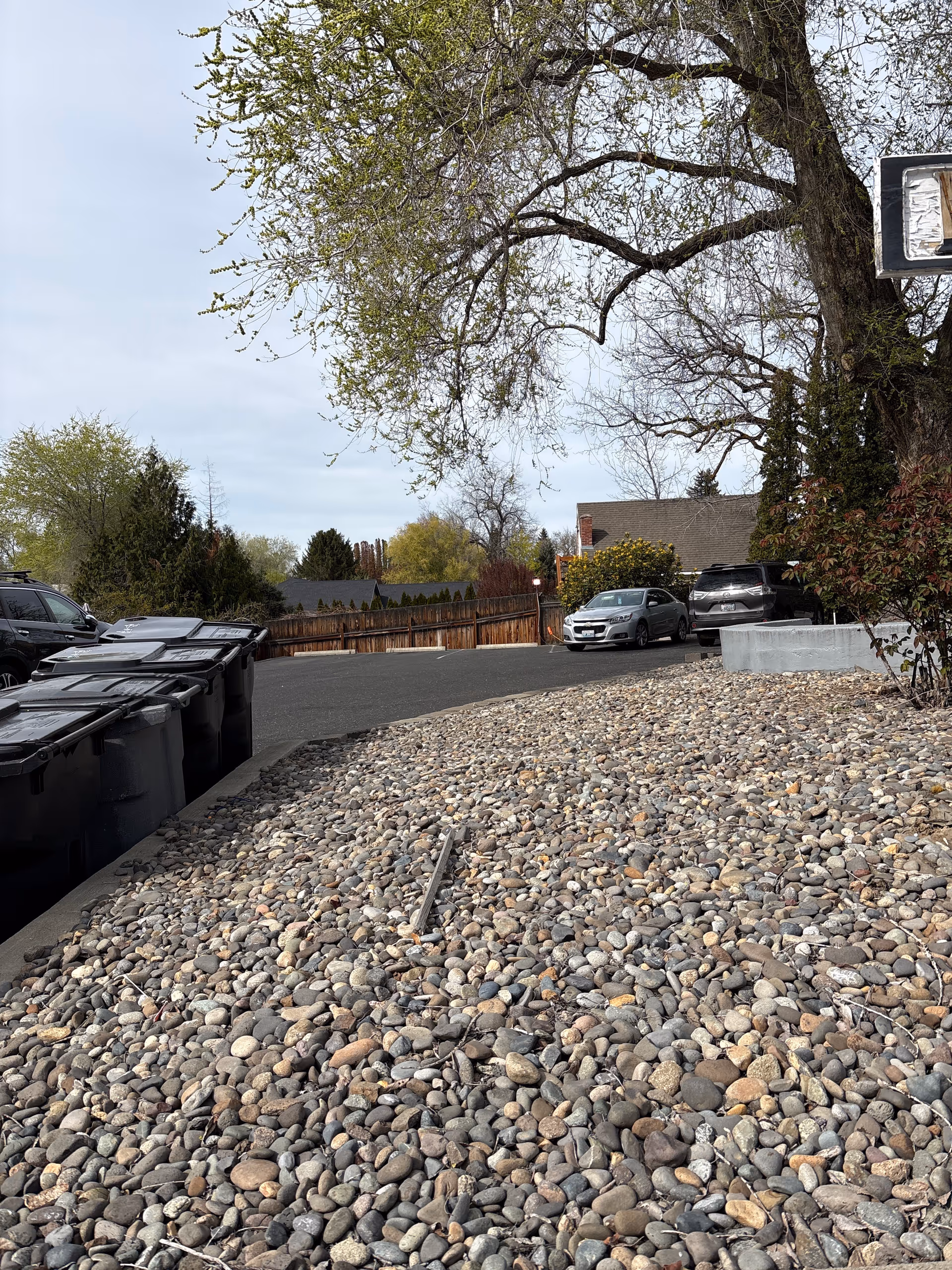 Exterior view of a gravel lot with parked cars and trash bins.