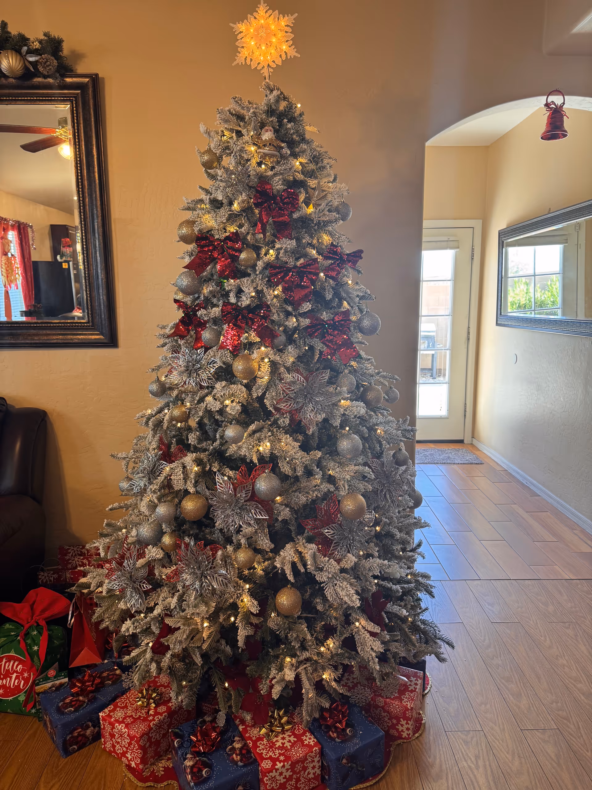 Tall frosted Christmas tree with red and gold ornaments inside a living room.