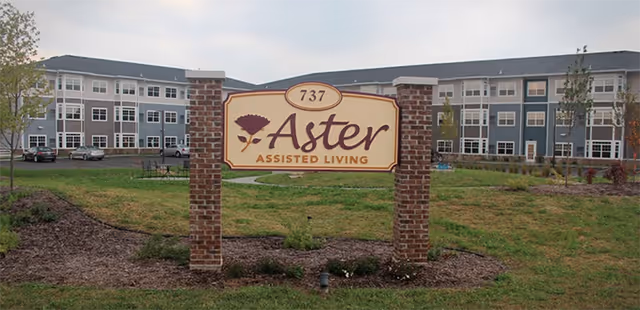 Exterior view of a senior living campus with a brick sign reading Aster Assisted Living.