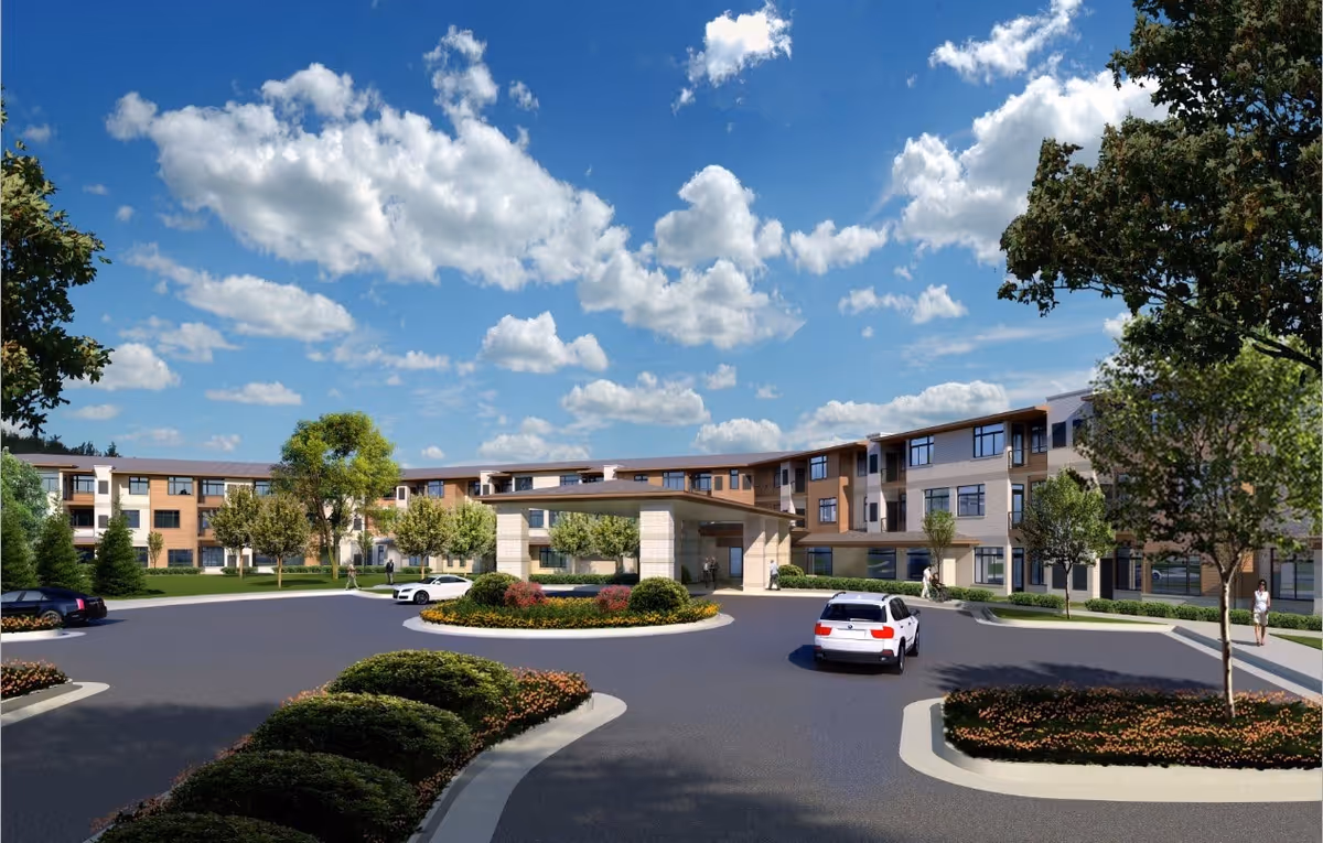 Front exterior of a three-story senior living building with a circular driveway, landscaped islands, and cars under a blue sky.