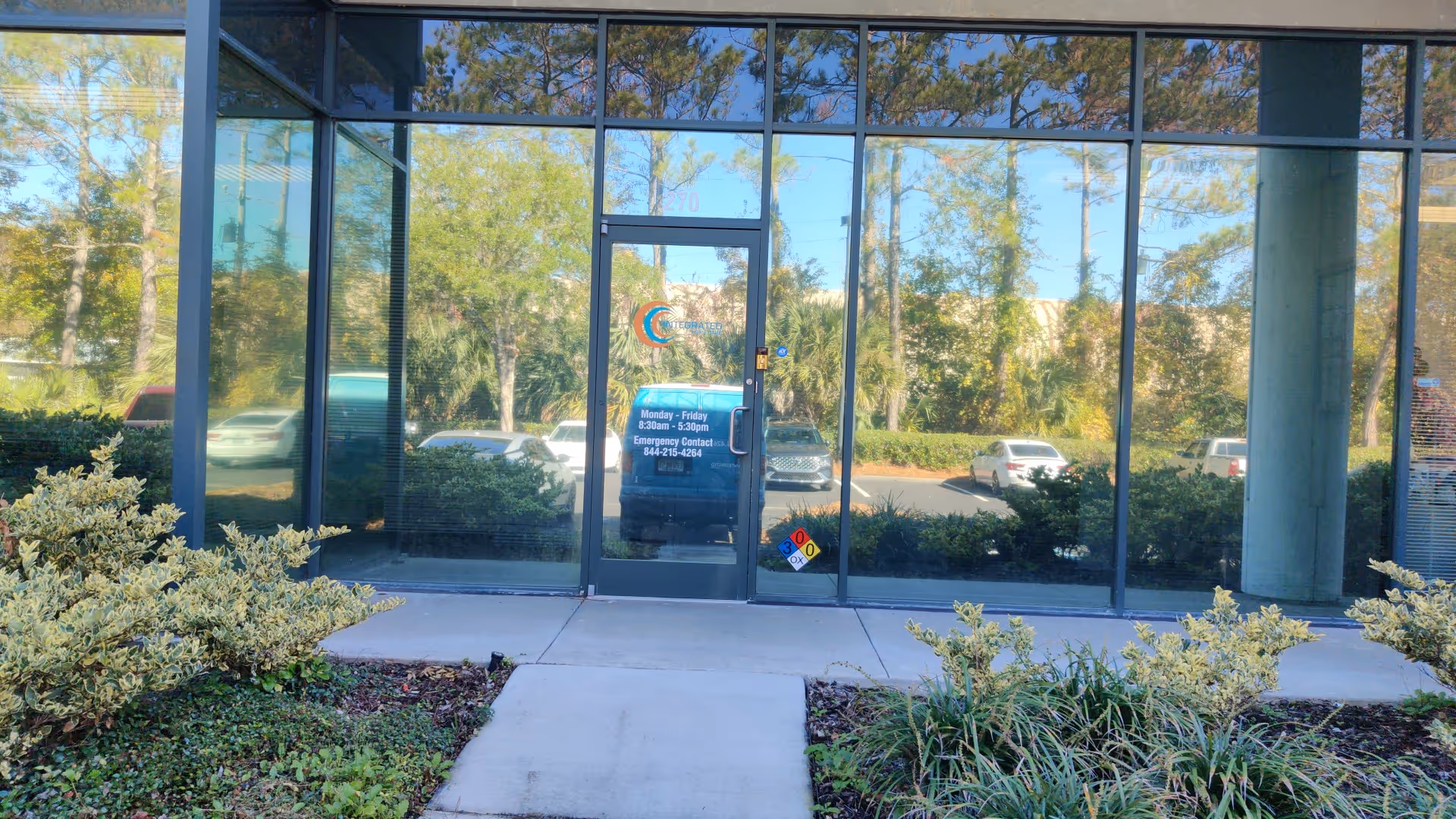 Glass-front entrance of a facility with reflective windows and landscaping in front