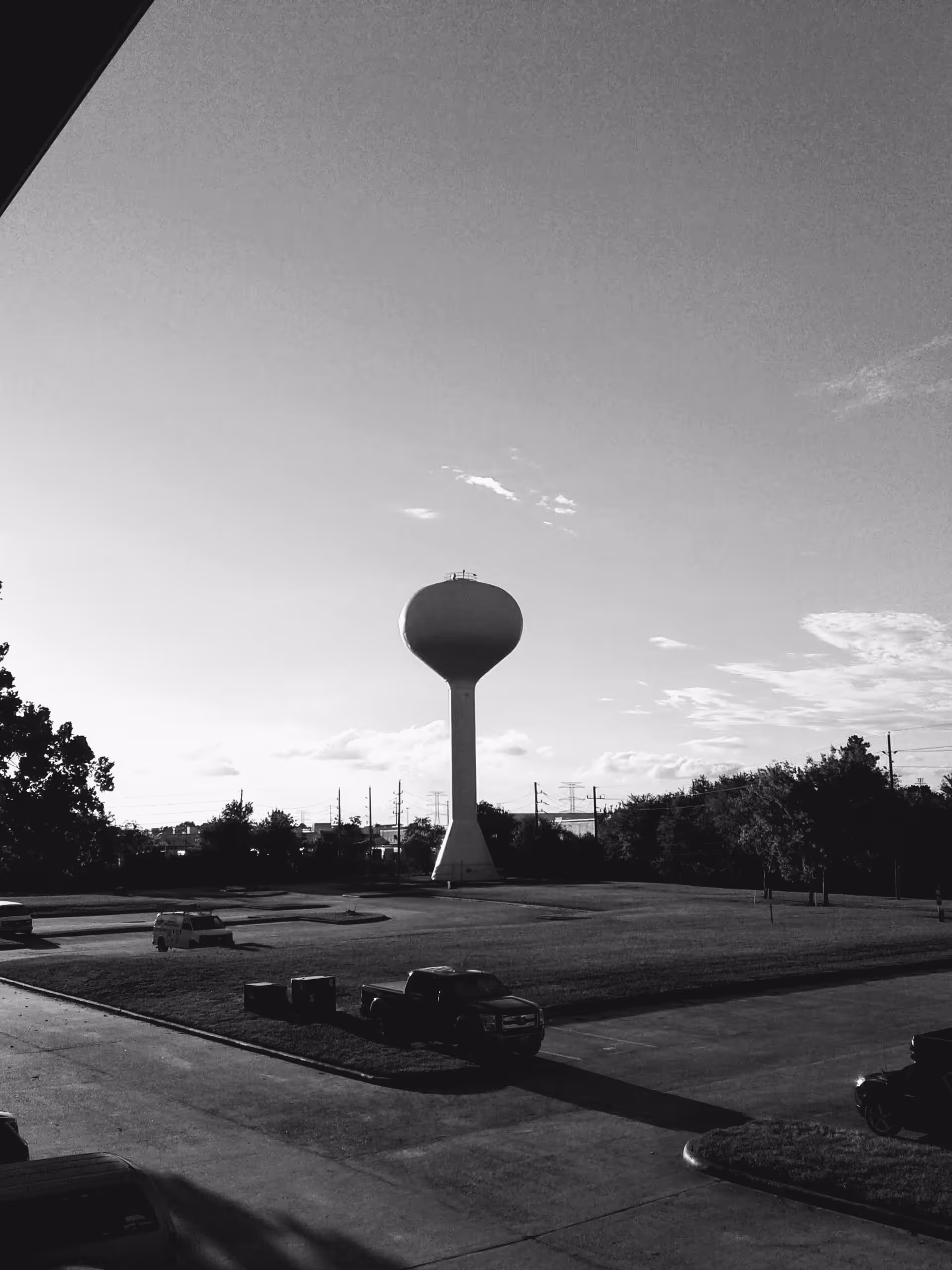 Outdoor exterior view of a water tower, parking lot, and trees.