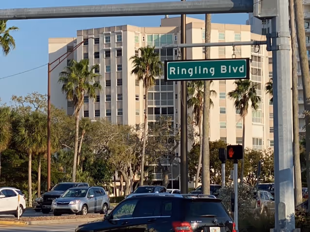 Exterior view of a tall beige building along Ringling Blvd with palm trees and cars.