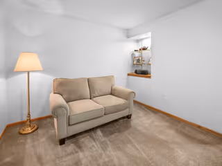 Small living room with beige sofa, floor lamp, and carpeted floor.