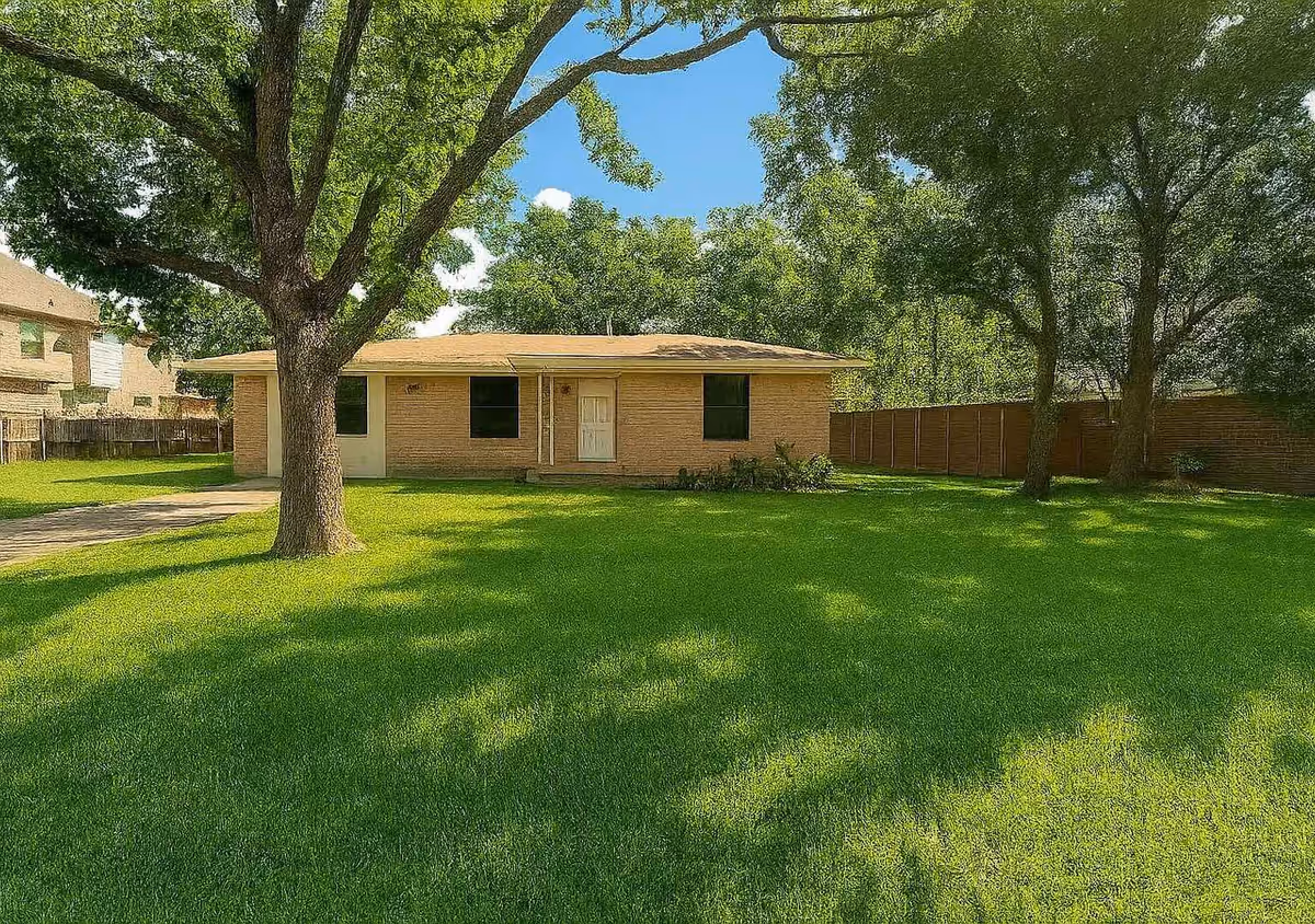 Single-story brick building with a green lawn and large trees in a fenced yard.