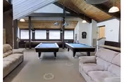 Recreation lounge with two pool tables, cushioned seating, and vaulted wooden ceiling.