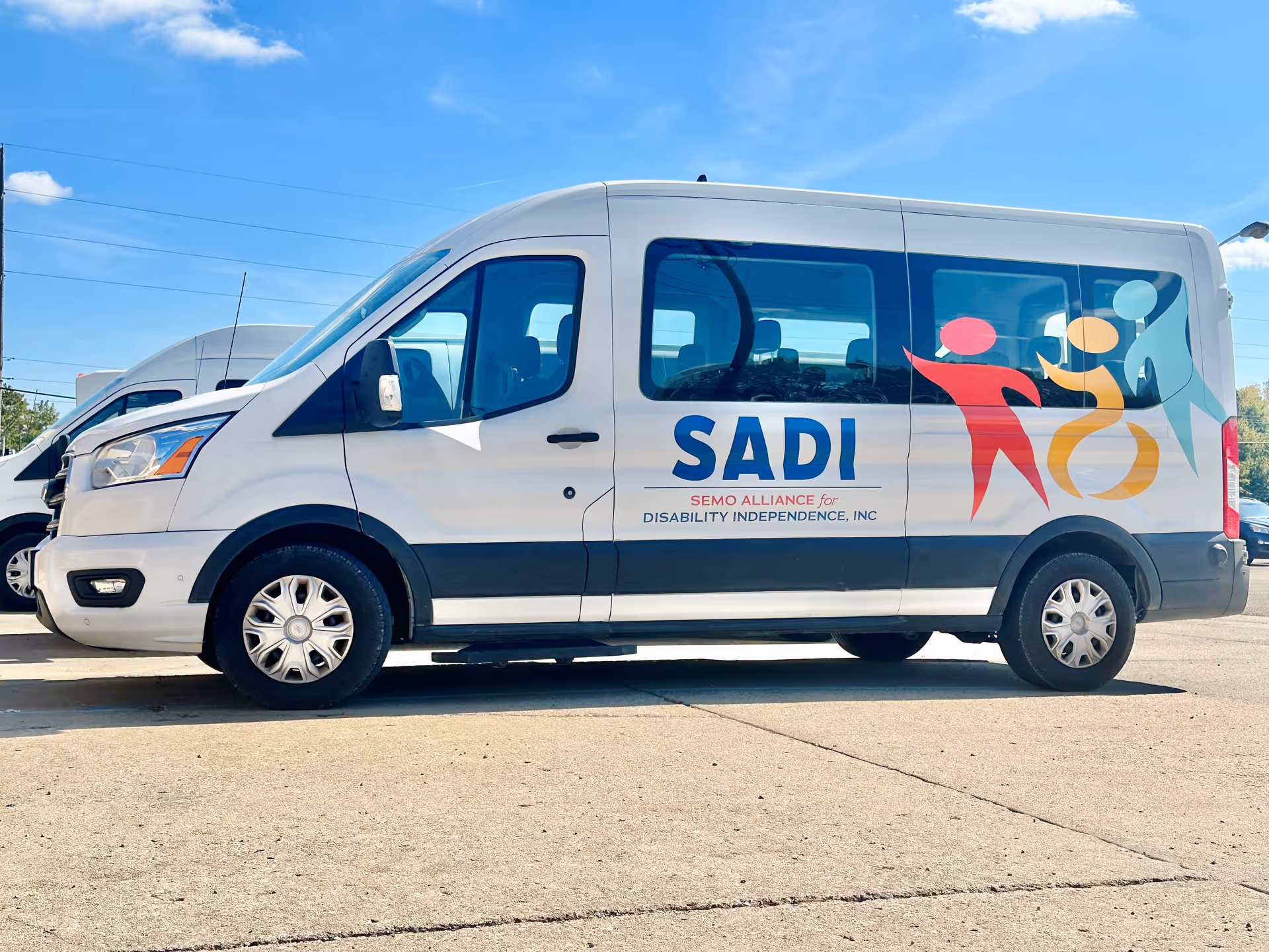 White transport van with SADI logo and colorful figures on its side.