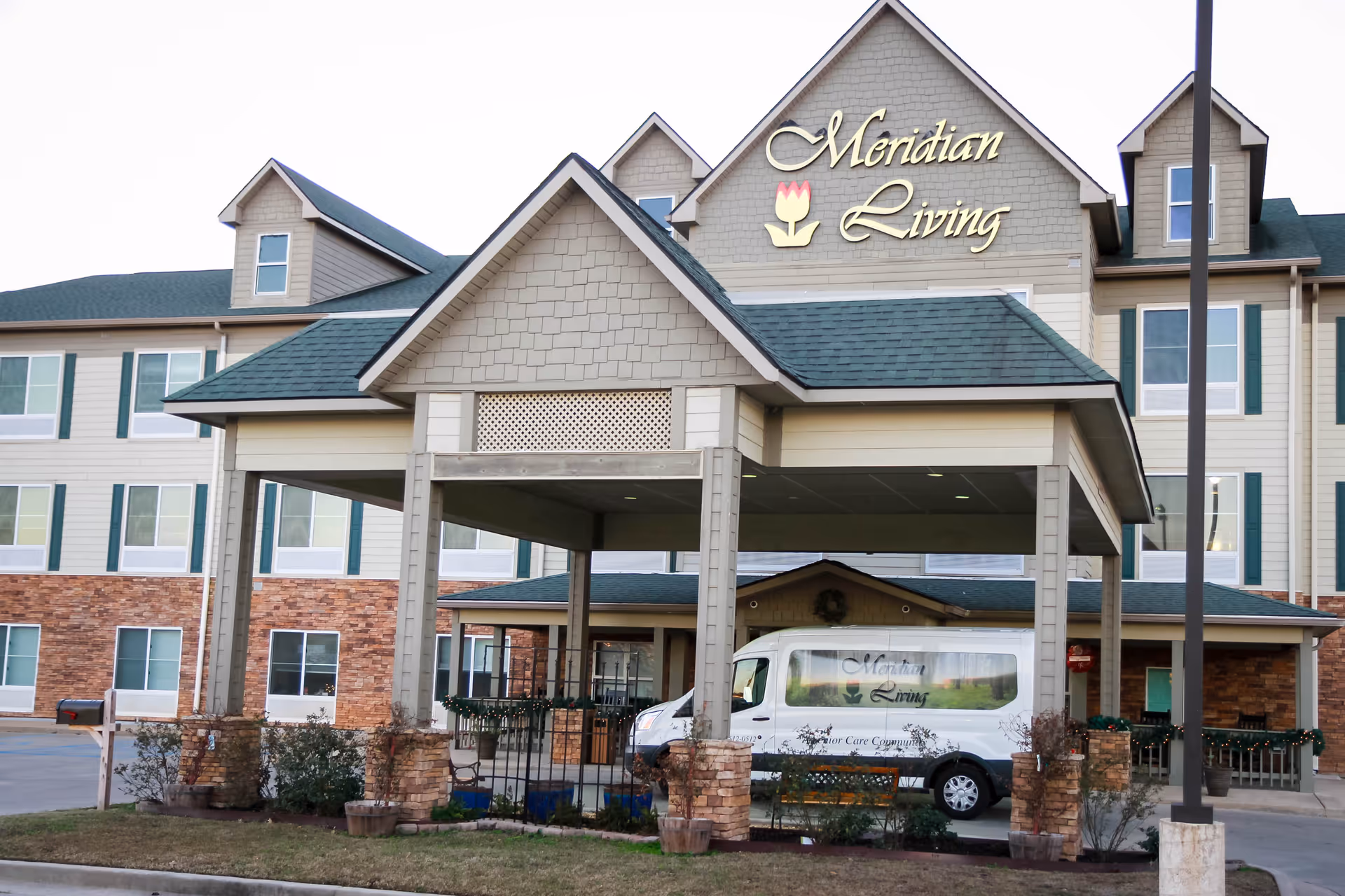 Exterior view of Meridian Living facility with porte-cochere entrance and branded van