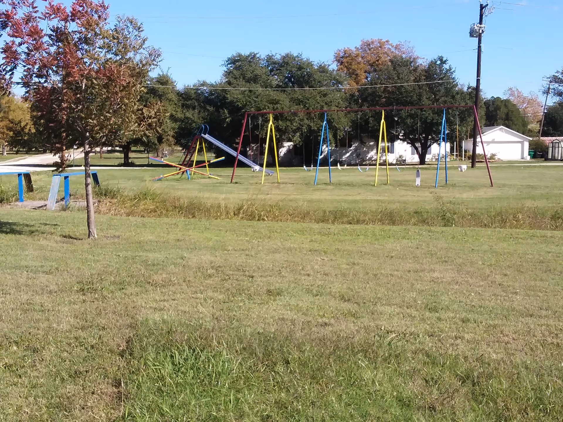 Open grassy park with colorful playground swings and a slide.