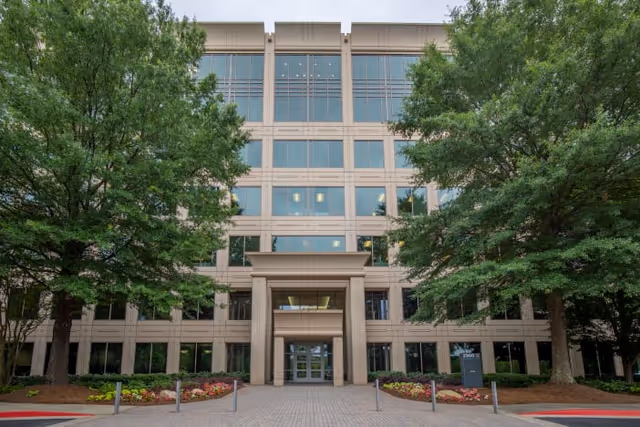 Front view of a modern senior living facility entrance, surrounded by trees and landscaped walkways.