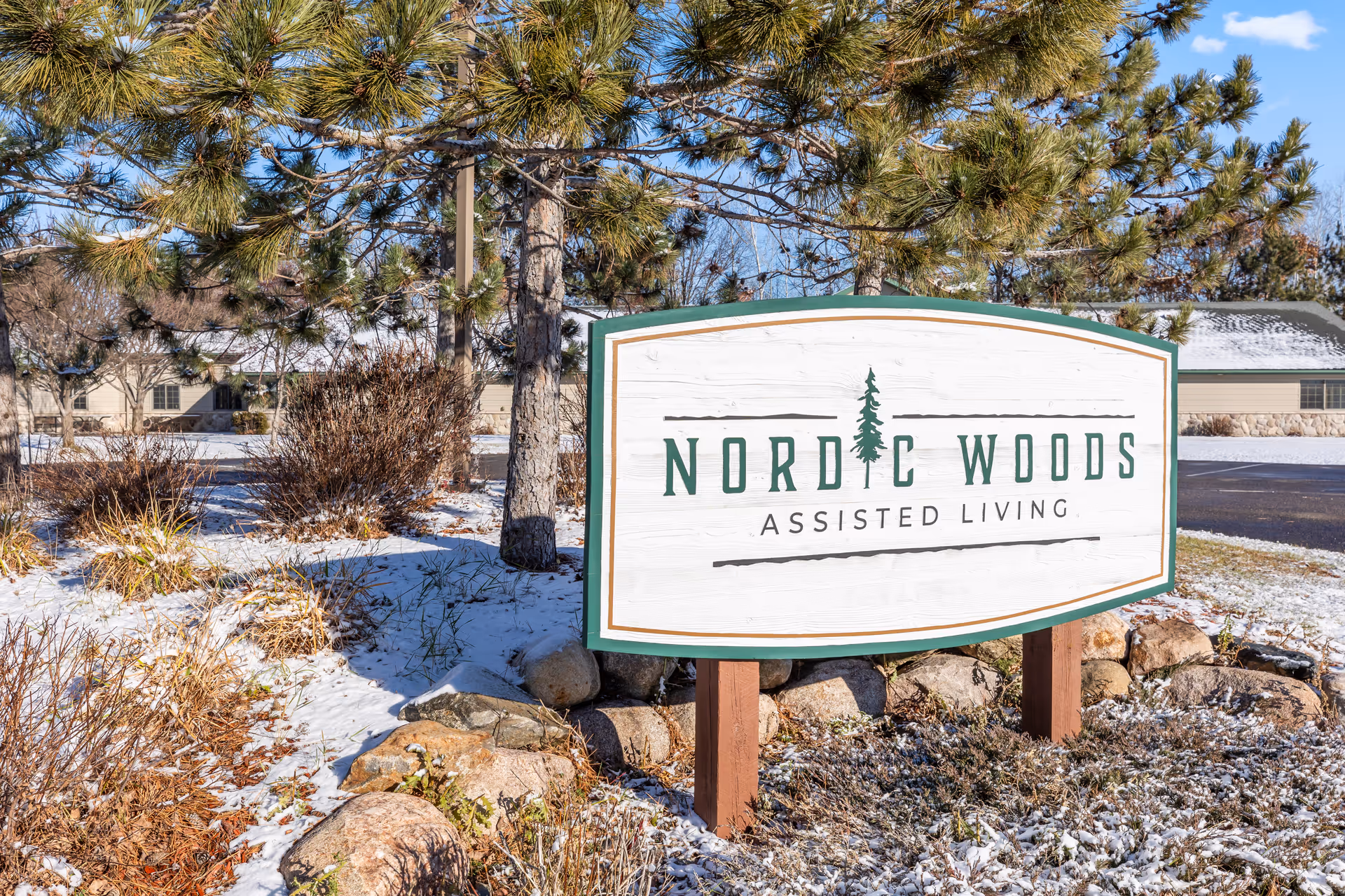 Nordic Woods Assisted Living sign in a snowy landscape with evergreen trees.