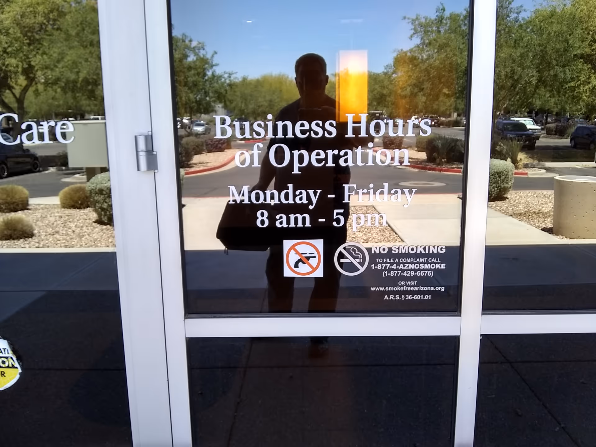 Glass door displays business hours with a reflection of a person outside.