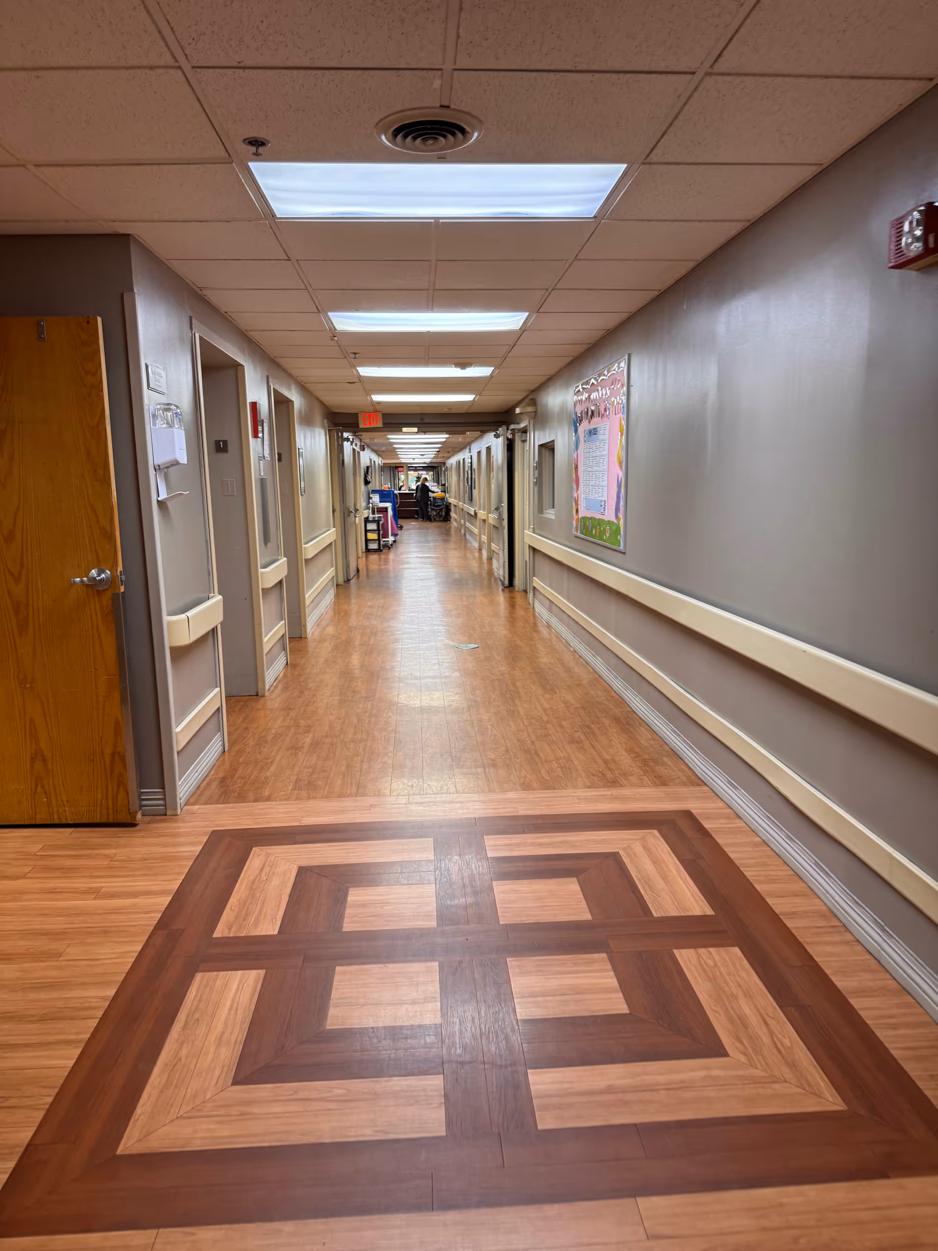 Long indoor hallway with wood-patterned floor and ceiling lights in a senior living facility