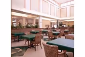 Bright dining hall with green tablecloth tables, chairs, and potted plants in an atrium.