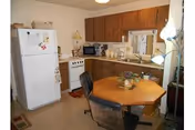 Small kitchen with refrigerator, stove, microwave, wooden cabinets, and a round dining table with chairs.