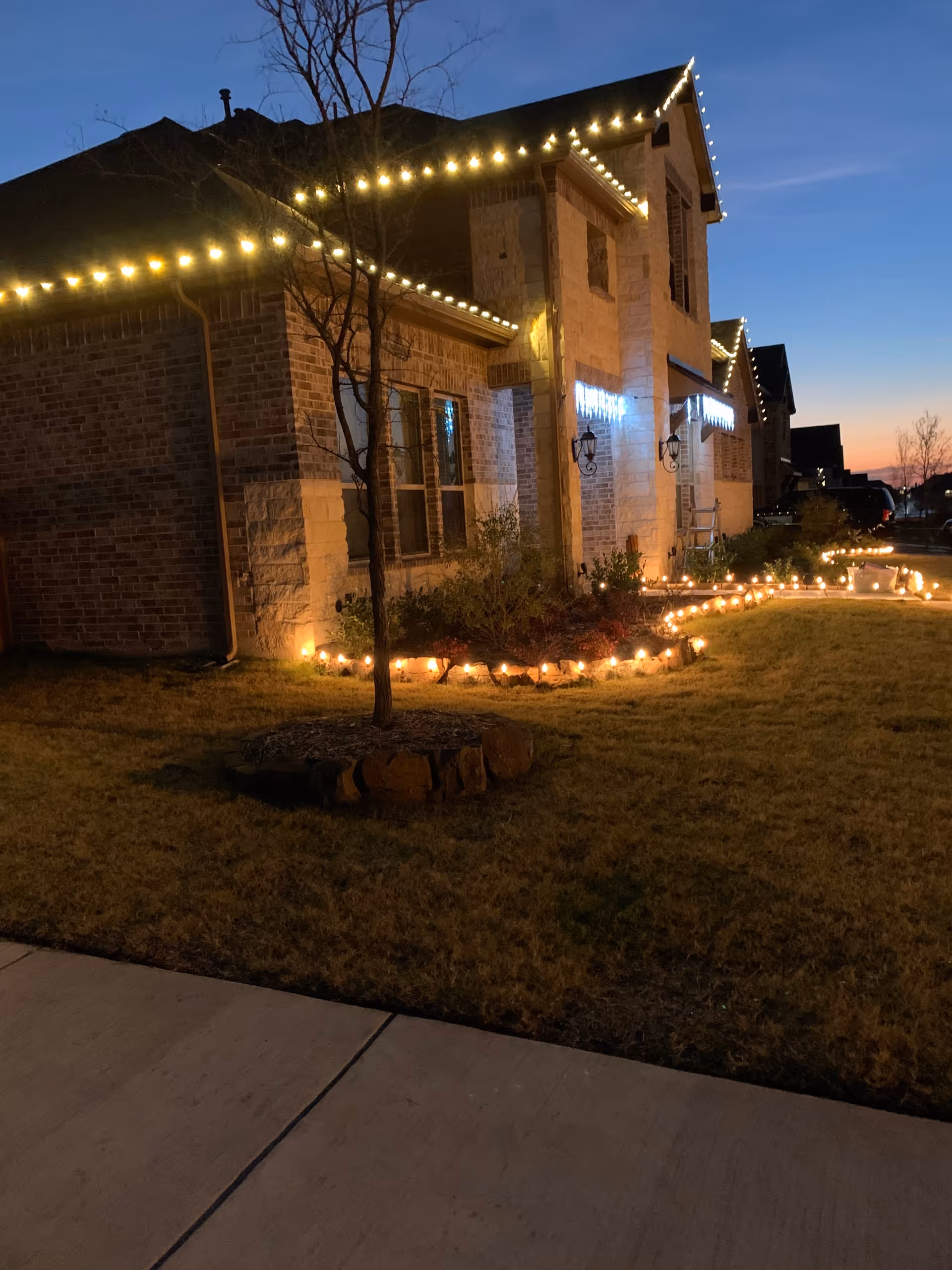 Night exterior of a brick senior living facility with decorative string lights along the roof.