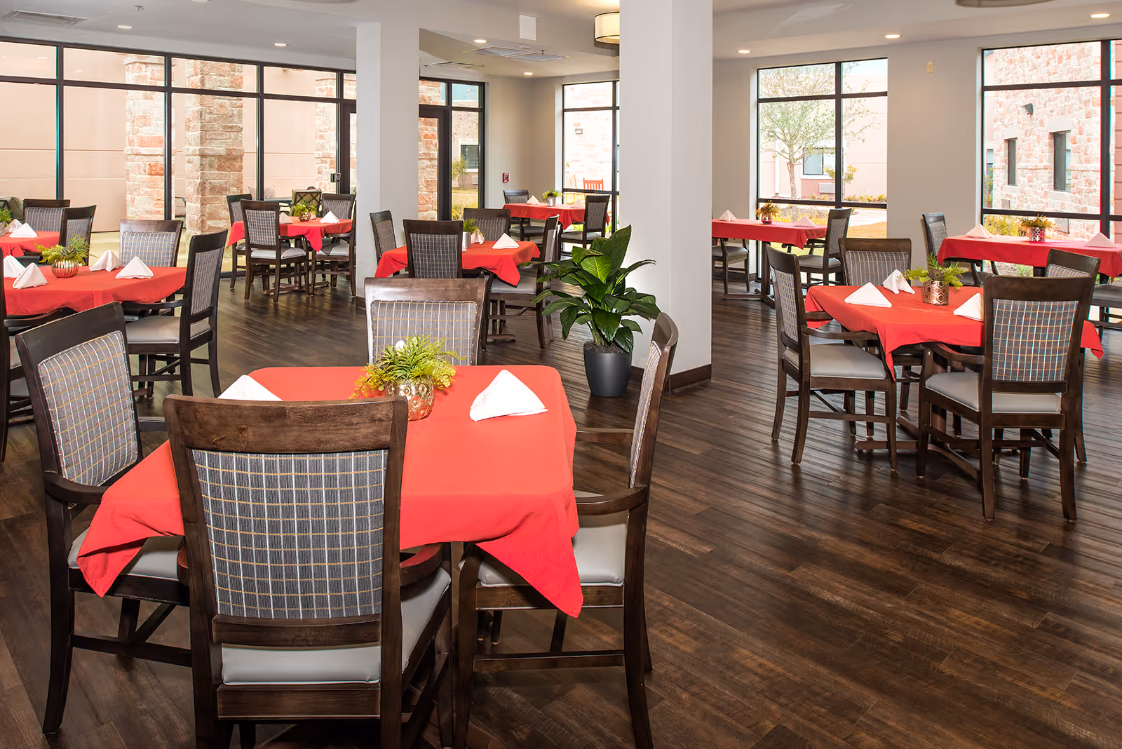 A spacious dining room with red tablecloths, chairs, and large windows.