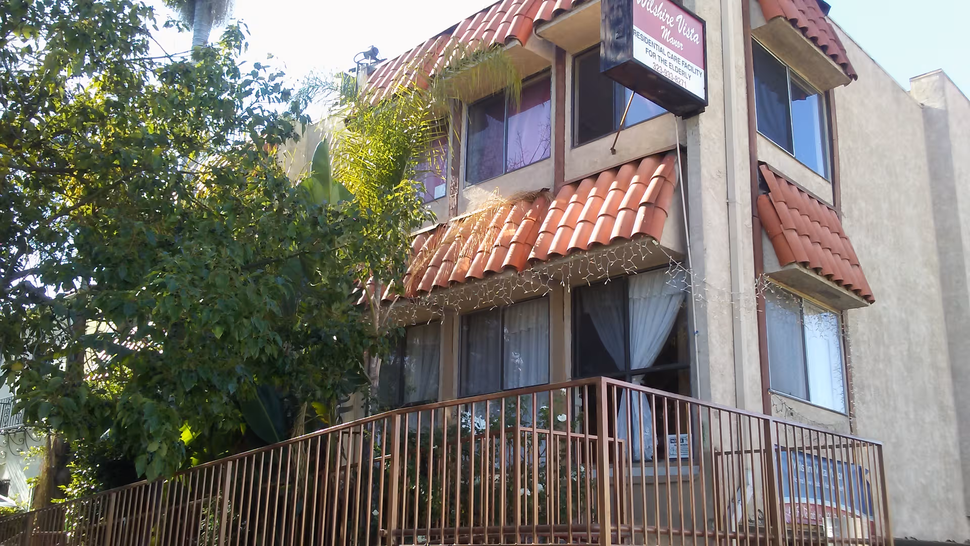 Exterior view of a two-story senior care facility with red-tiled roof and balcony.