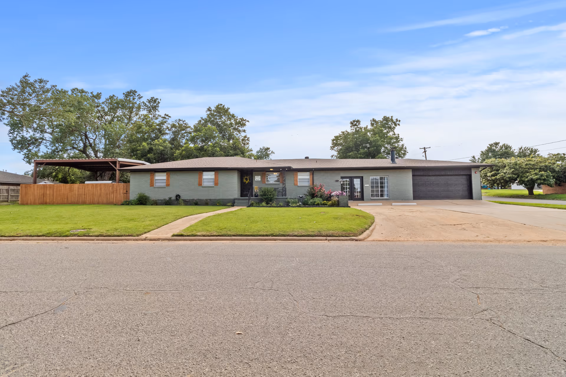 Single-story ranch-style building with green lawn, driveway, and trees in a suburban front yard.