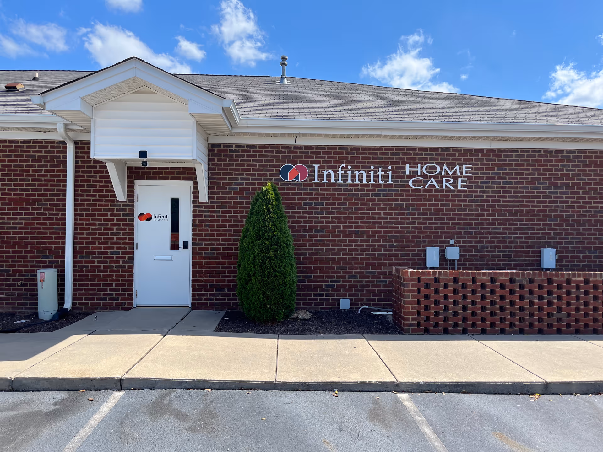Brick exterior of Infiniti Home Care facility with entrance door and a small evergreen shrub.