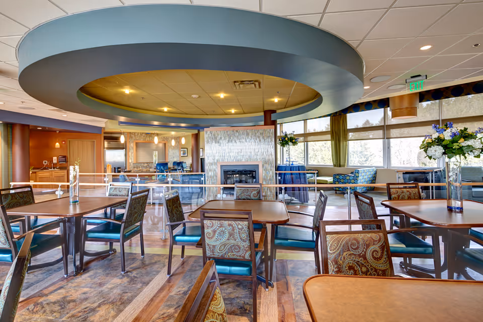 Modern senior living dining area with a circular ceiling feature, multiple tables, and lounge seating.