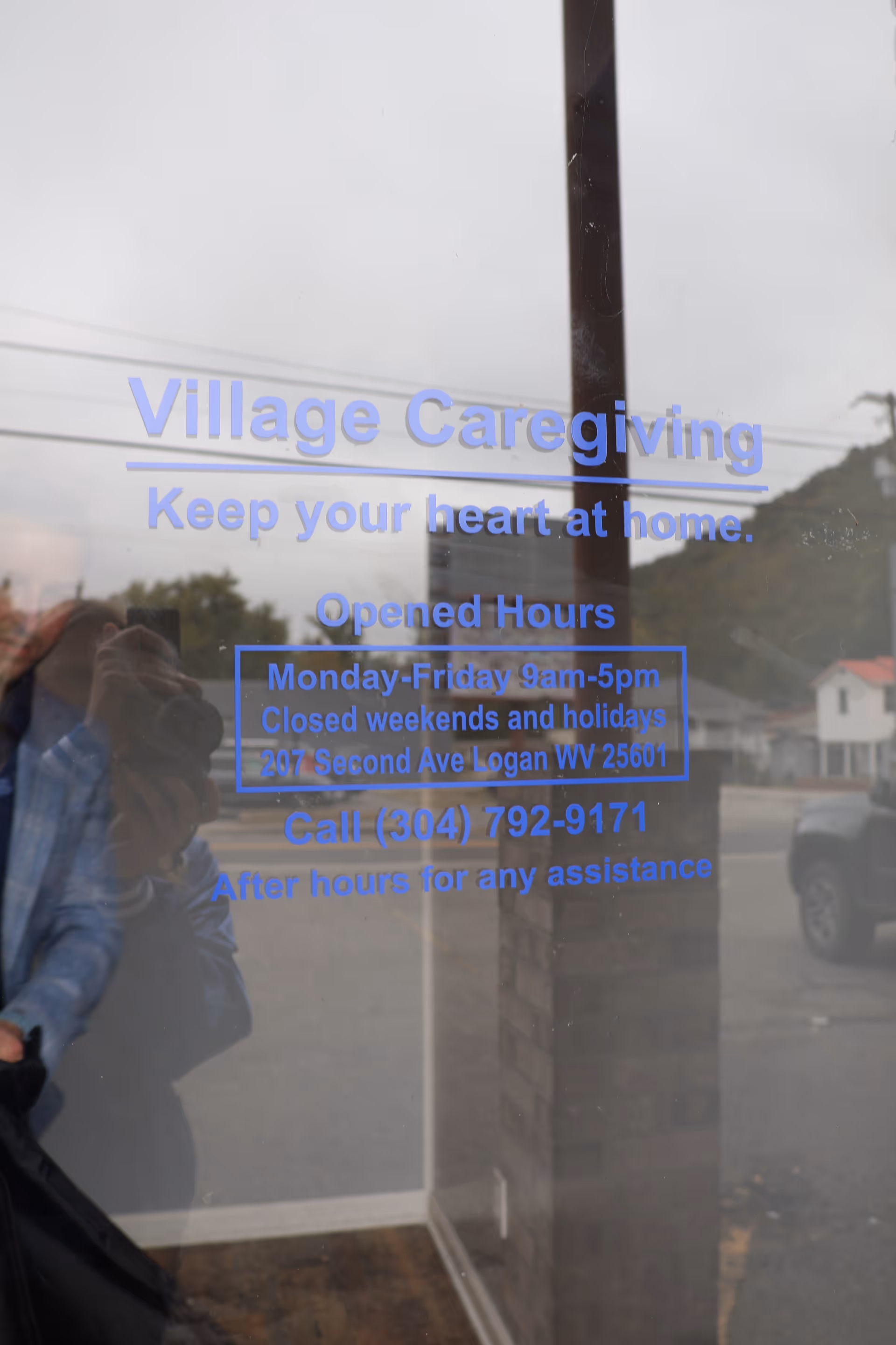 Glass door with blue Village Caregiving sign reflecting the street outside.