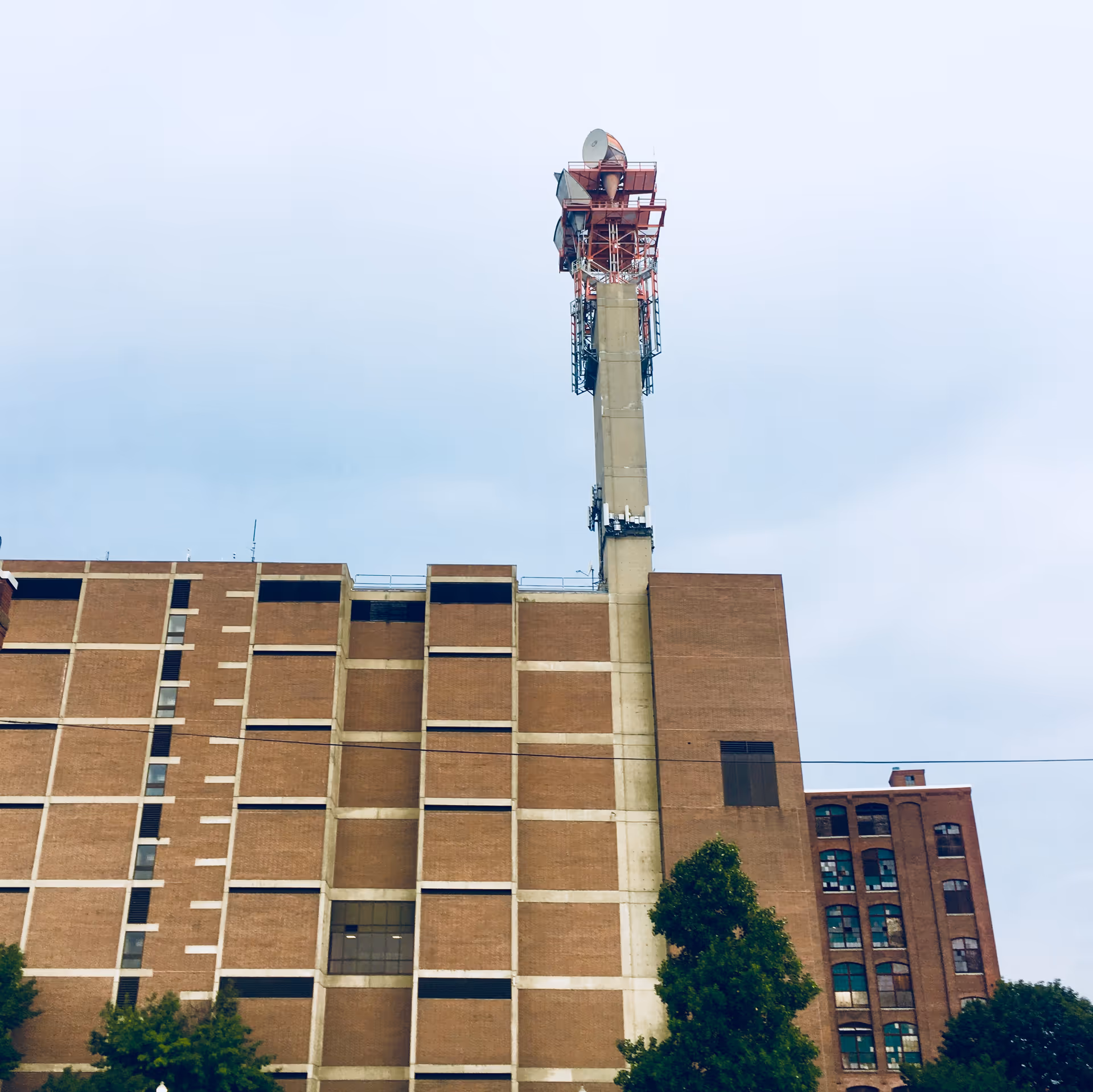 Tall brick building with a tower antenna against a cloudy sky.