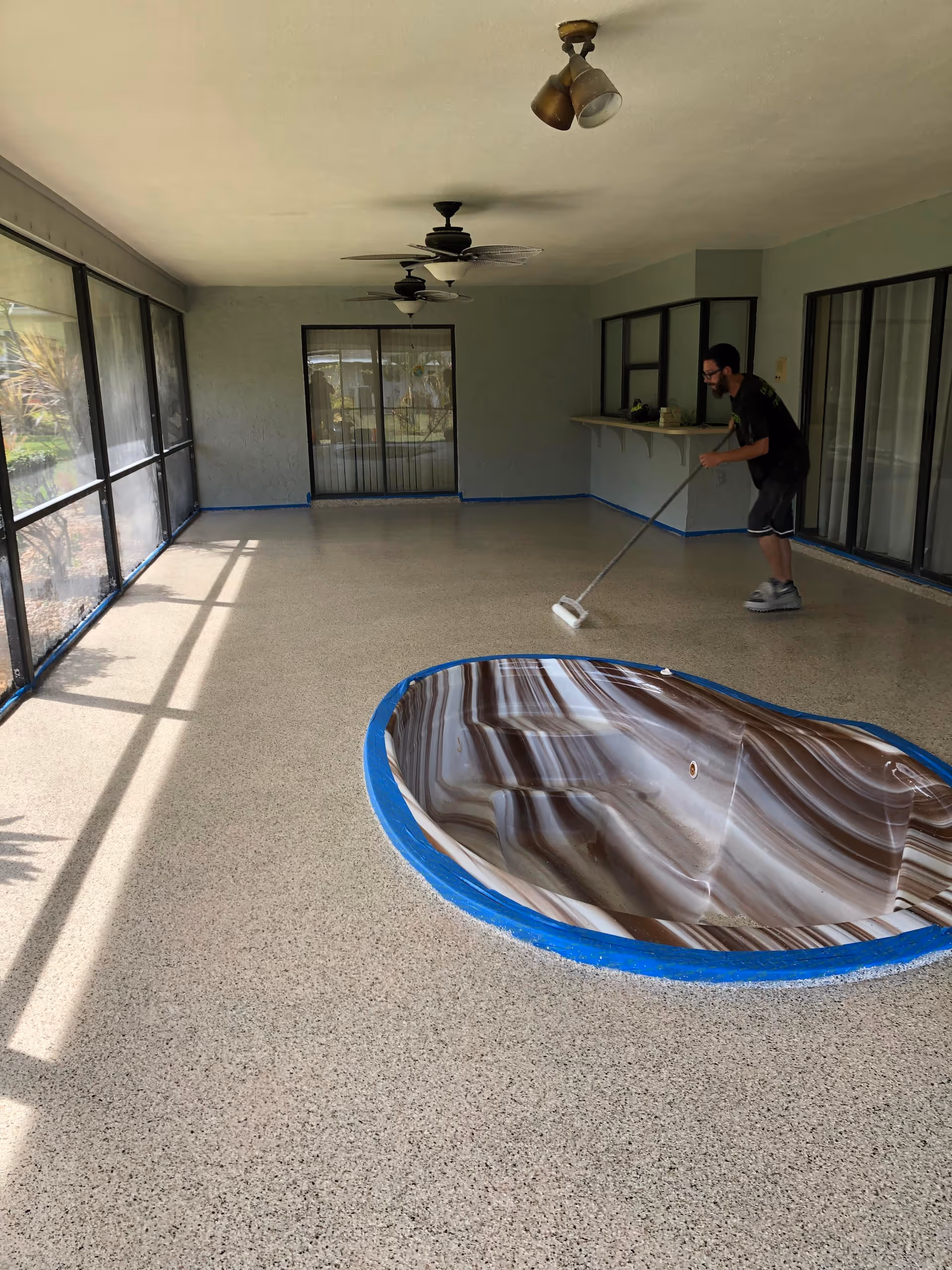 A person mops a large covered interior patio with ceiling fans and glass walls.