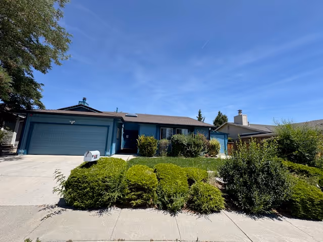 Single-story blue residential care building with driveway, garage, and landscaped front yard.