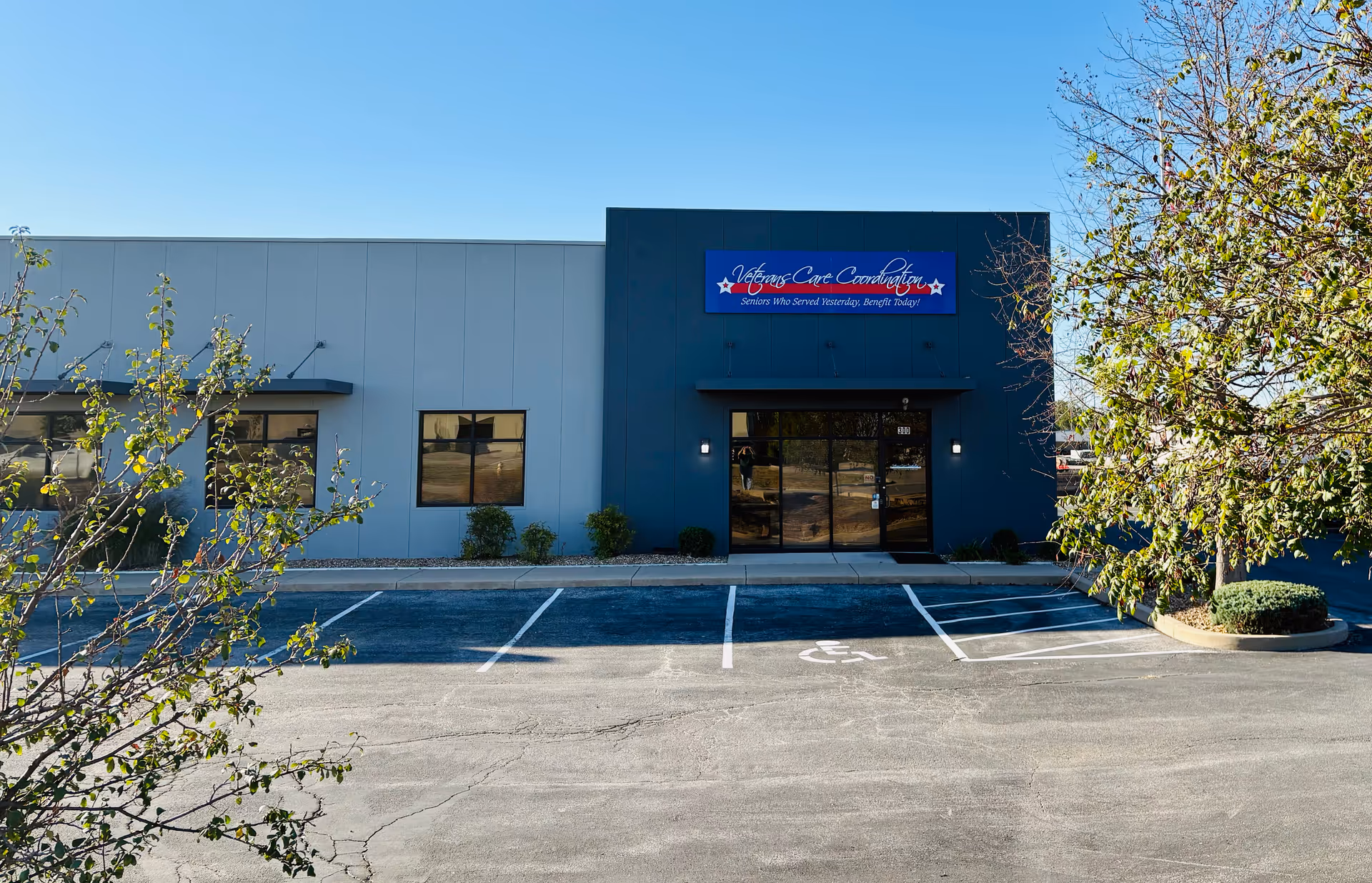 Exterior of a single-story facility with a blue sign above glass doors and the parking lot.
