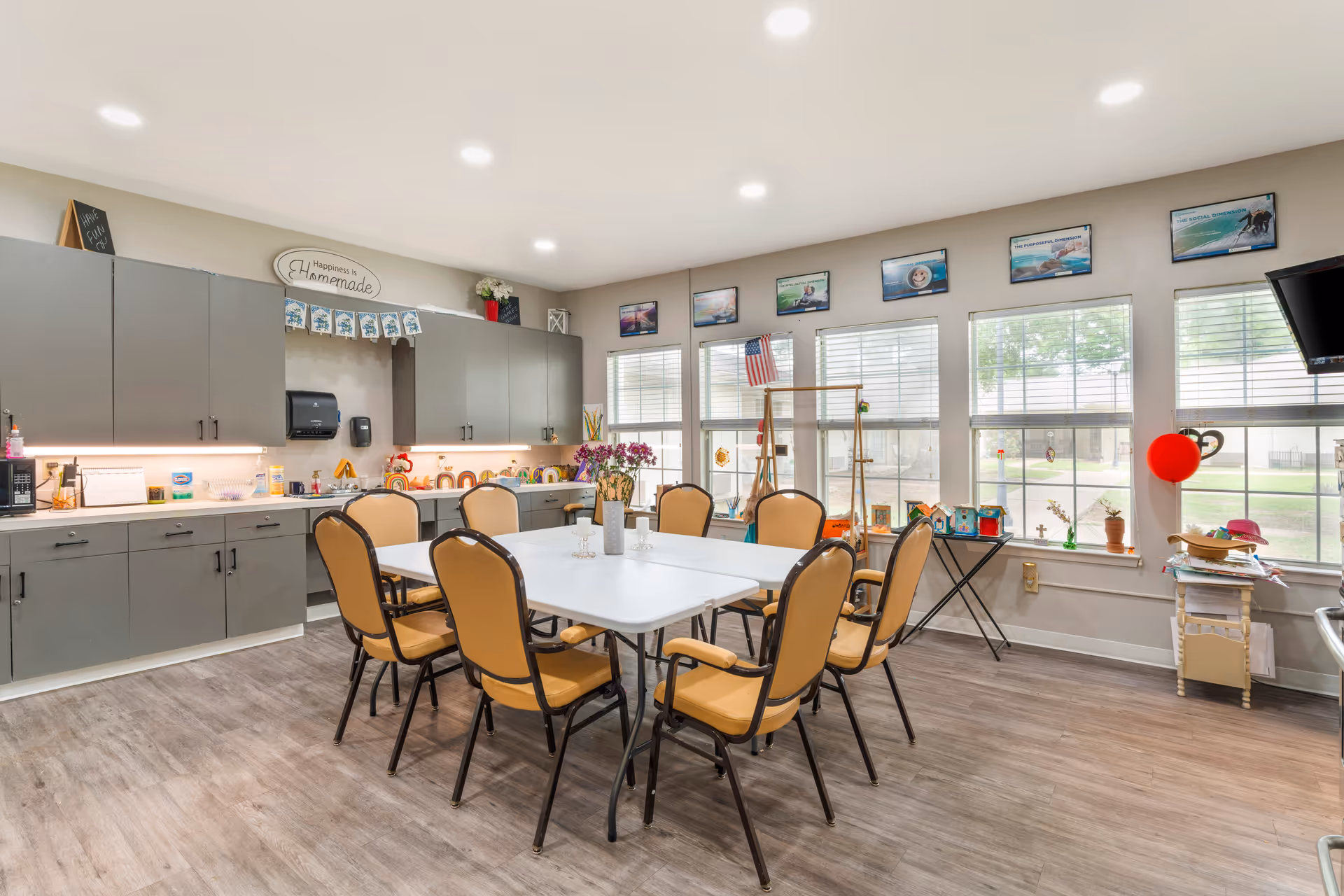 Senior living facility dining area with gray cabinets, white table, and tan chairs.