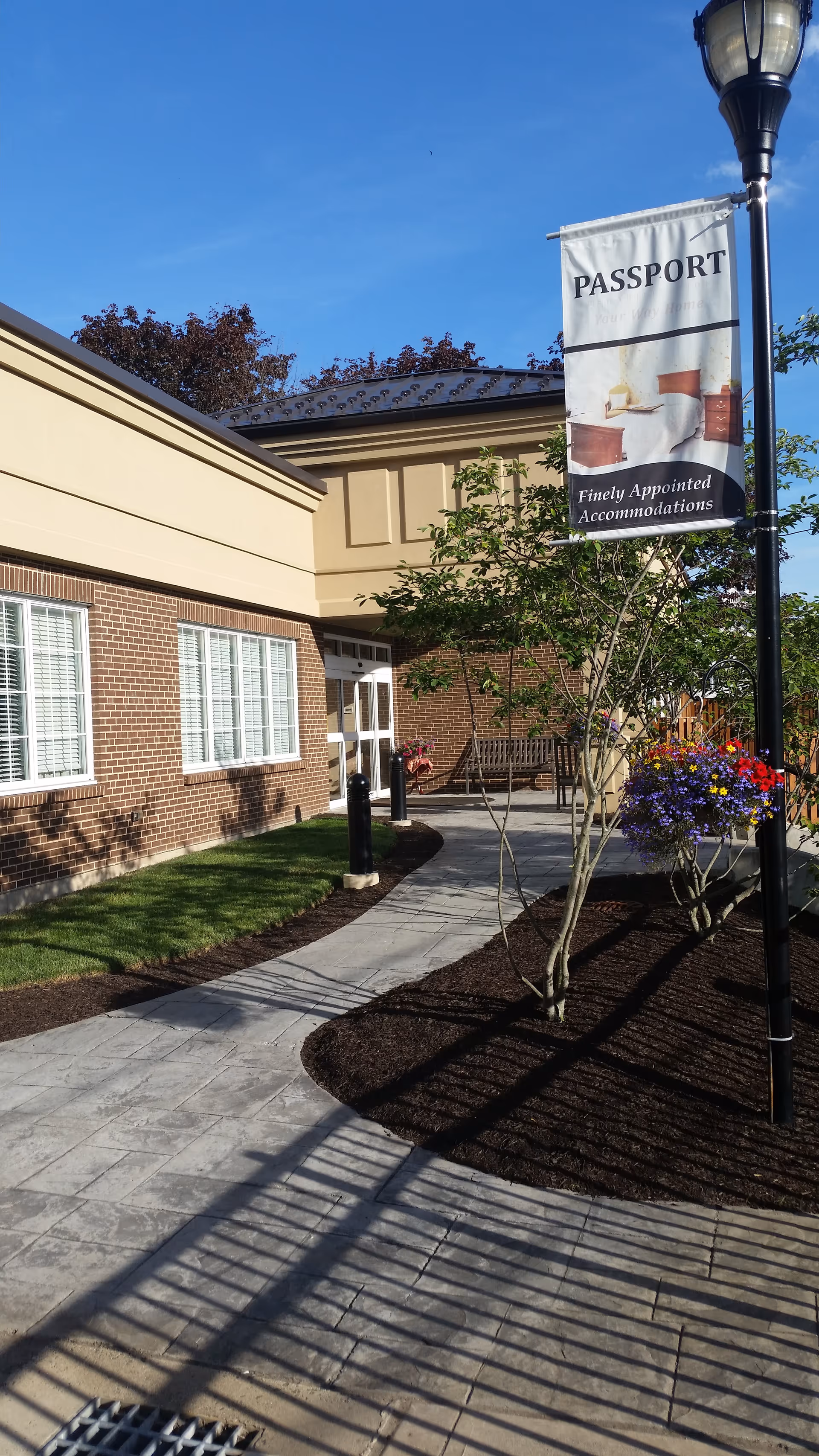 Exterior view of a brick senior living facility with a banner and paved walkway.