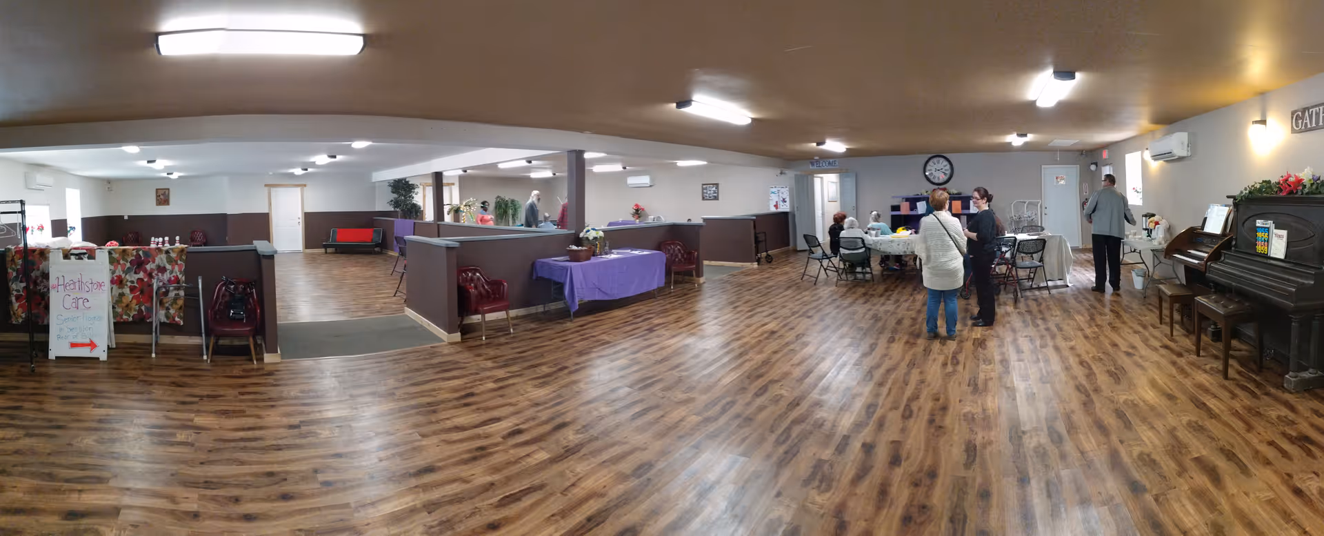Spacious senior living common area with seating, tables, and a piano.