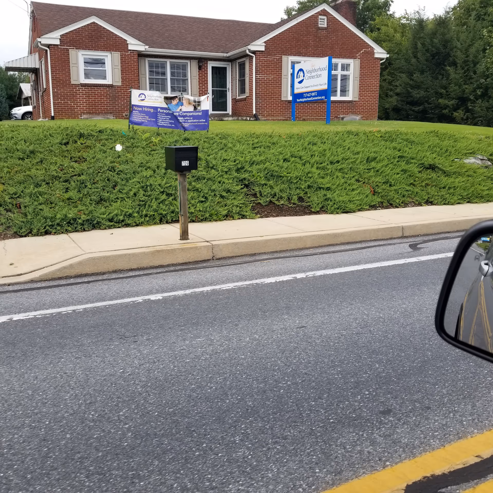 Brick senior living facility exterior with lawn banners, sign, and a sidewalk along the street.