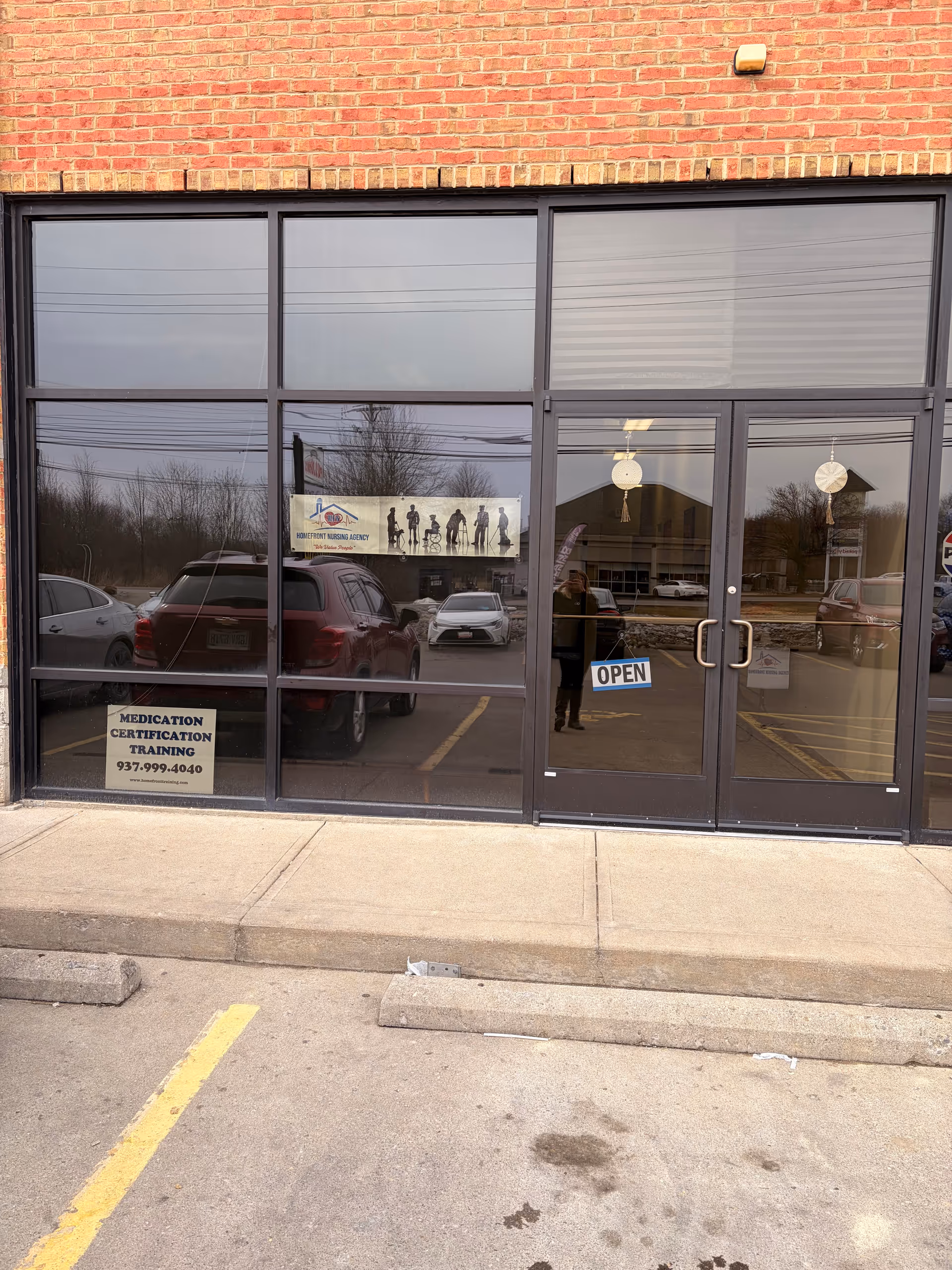 Brick storefront with large glass doors, Open sign, and a Homefront Nursing Agency sign.