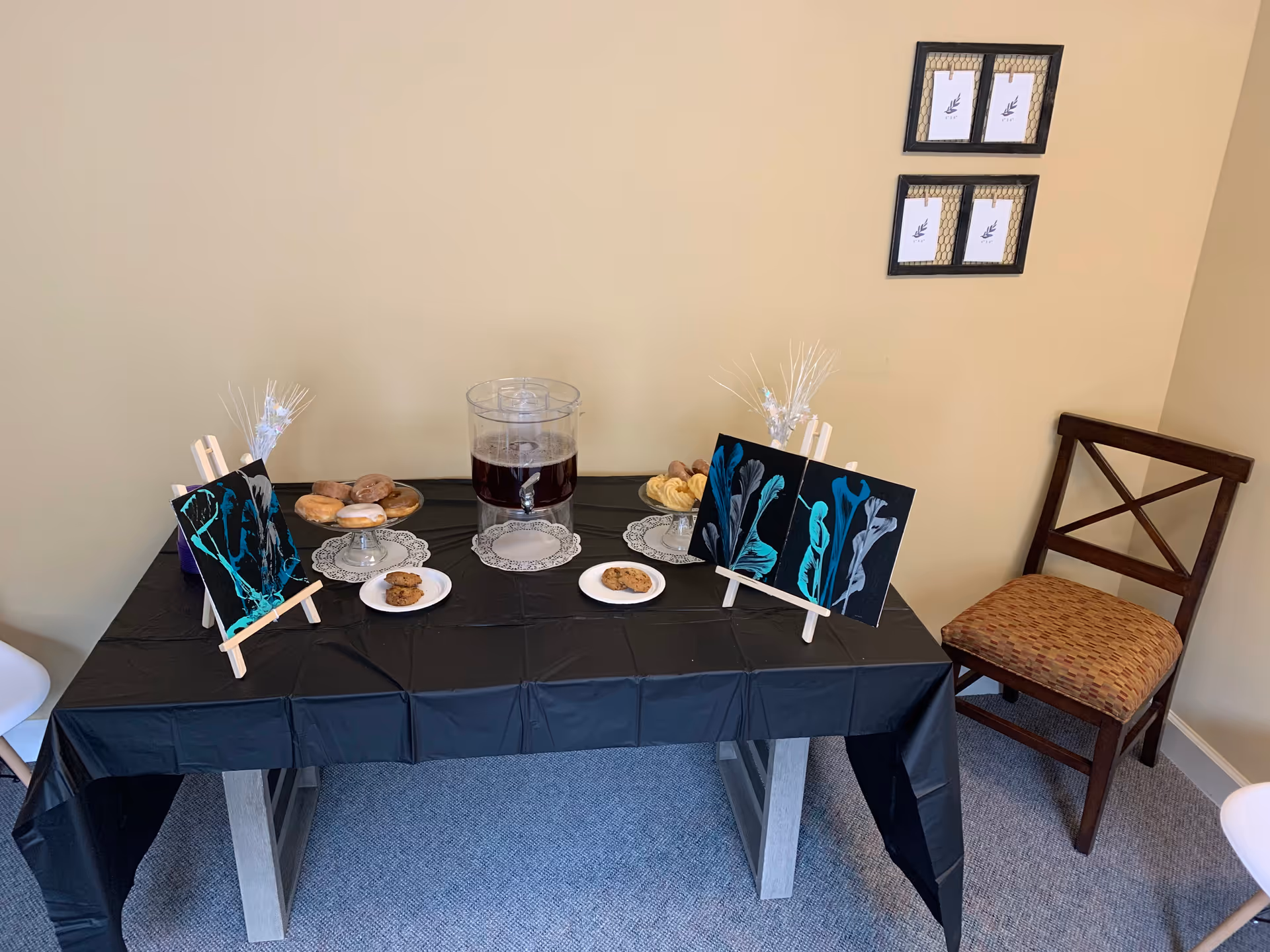 Dining table with black tablecloth, pastries, and beverage dispenser in a corner of a room.