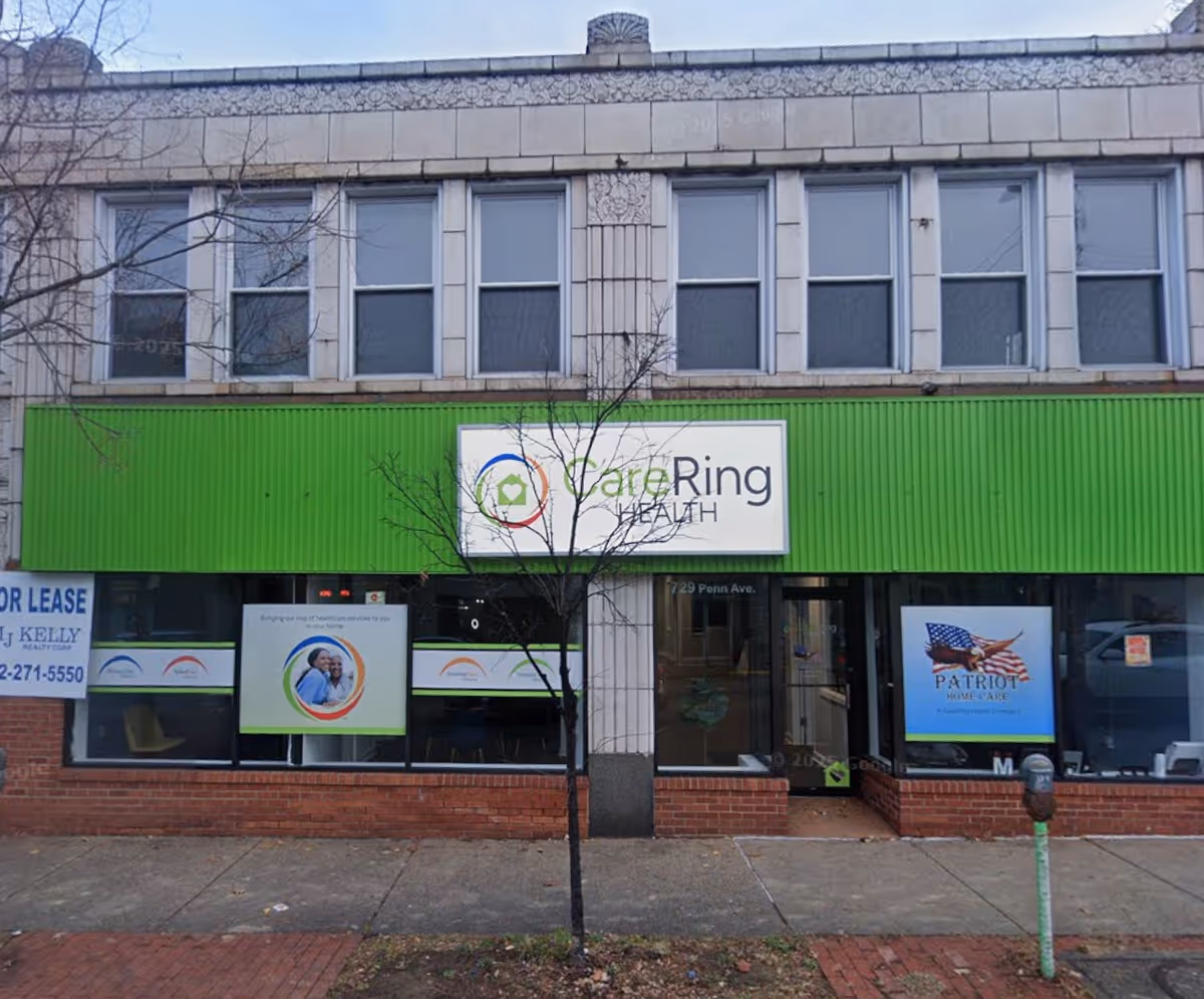 Street-level view of a two-story building with bright green storefront signage and Patriot Home Care posters.