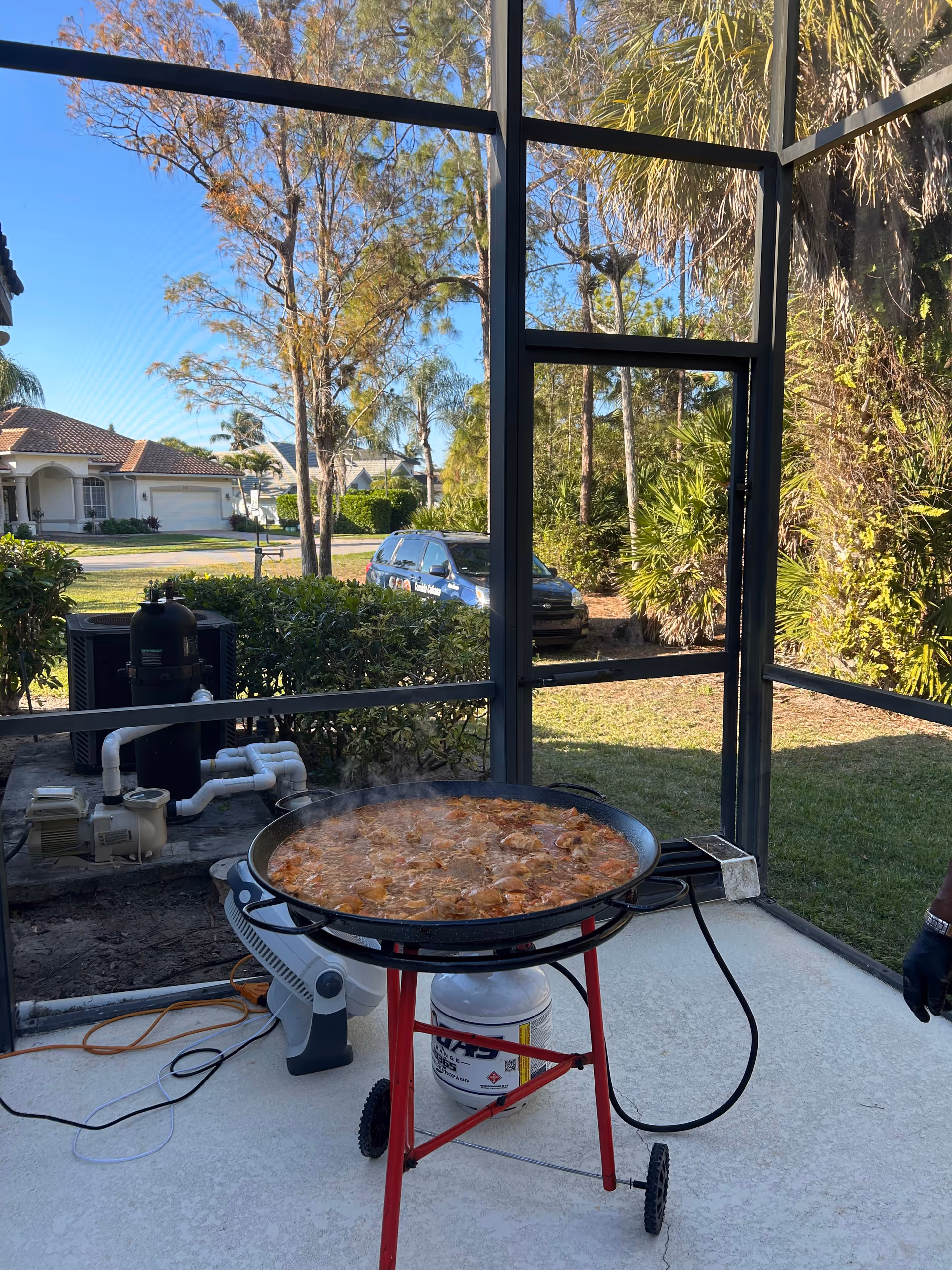 Large paella pan on a stand cooking outdoors in a screened patio area.