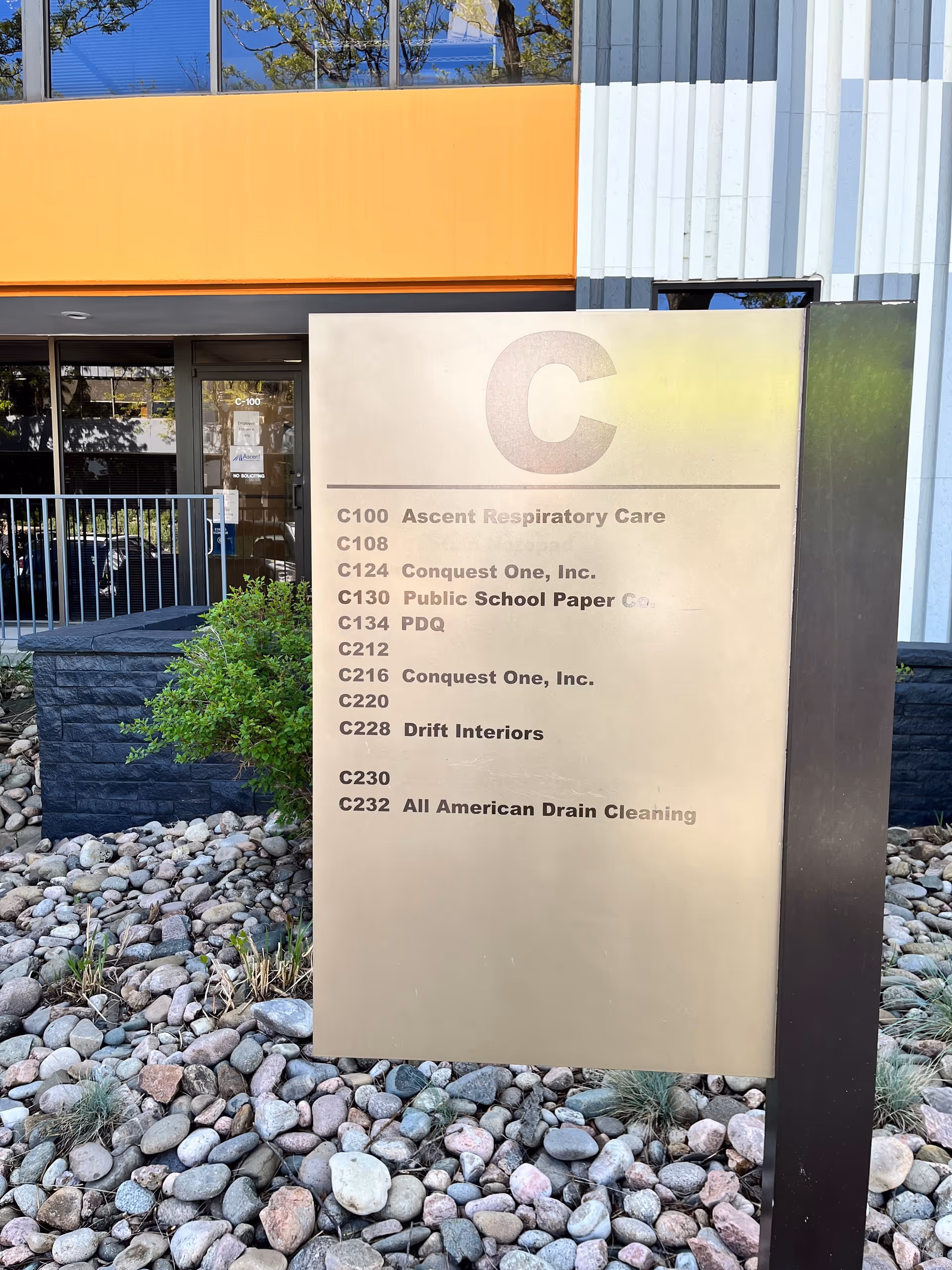 Exterior building entrance with a metal directory sign and rock landscaping