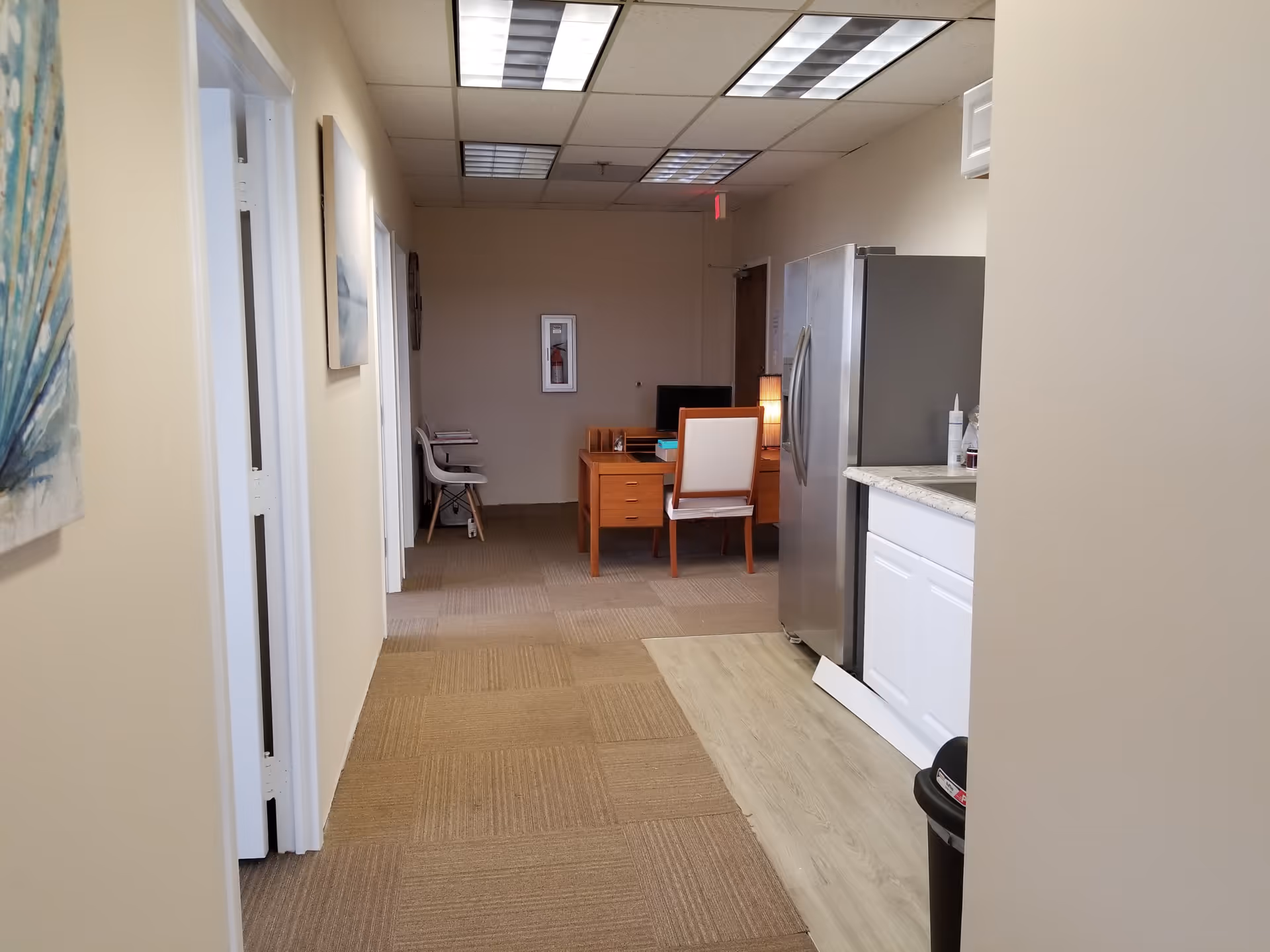 Hallway in a senior living facility leading to a small office and kitchenette area.