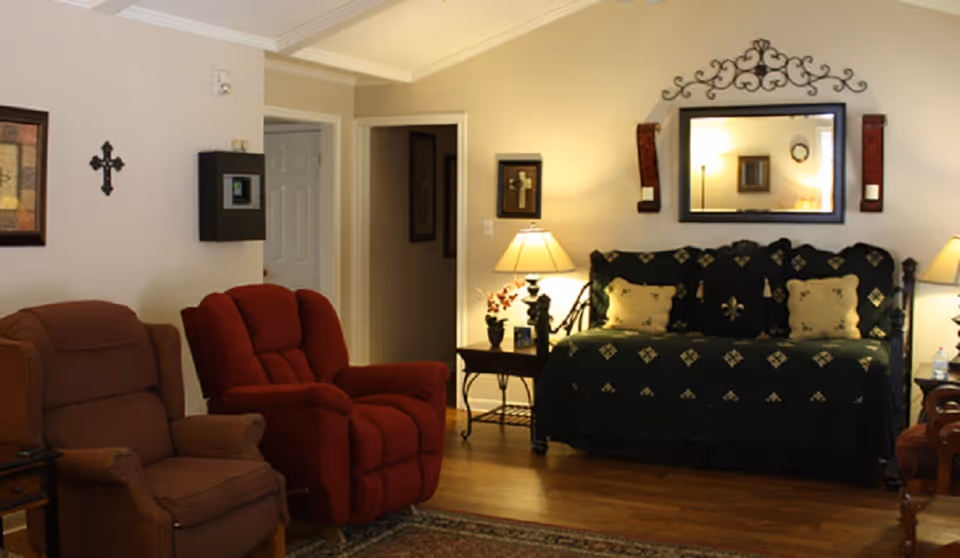 Cozy living room in a senior care facility with recliners, a bed, and warm lighting.