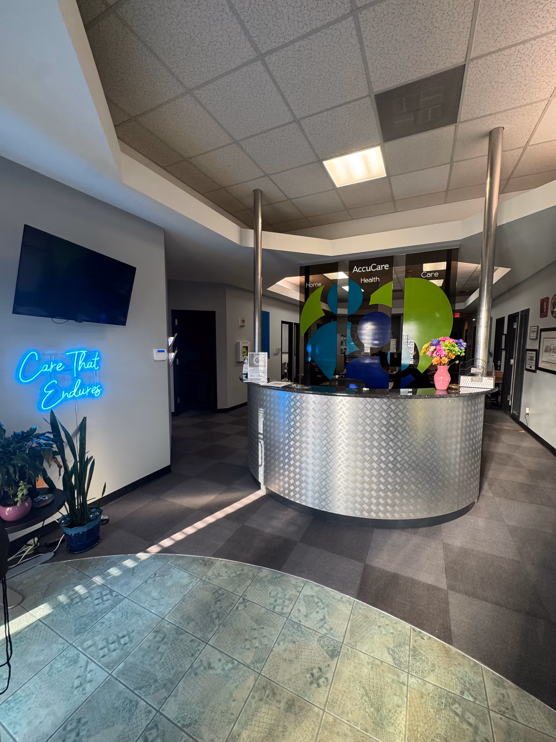 Curved metal reception desk in a modern AccuCare lobby with neon sign and plants.