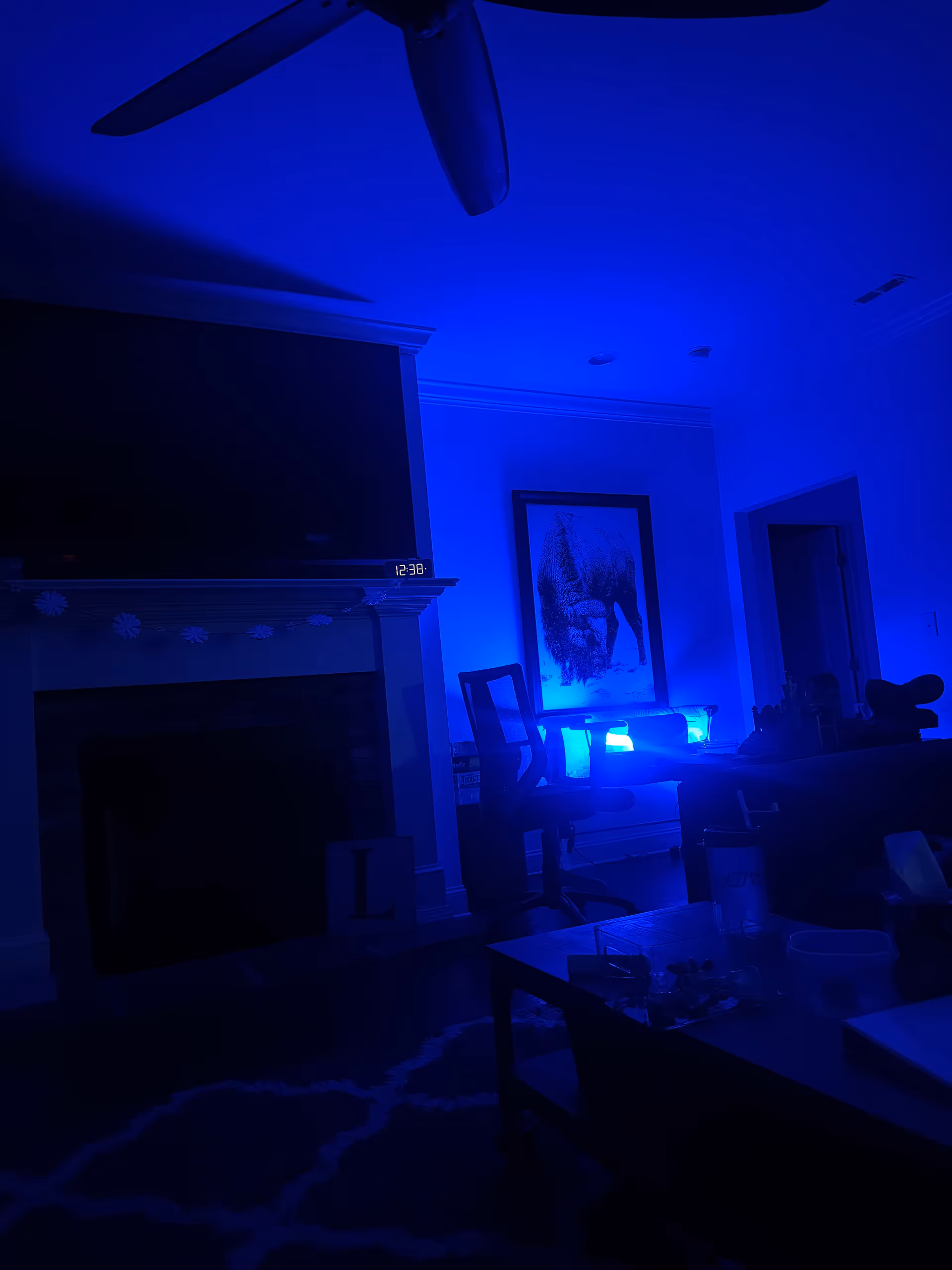 Blue-lit living room with fireplace, TV, chair, and framed wall art.