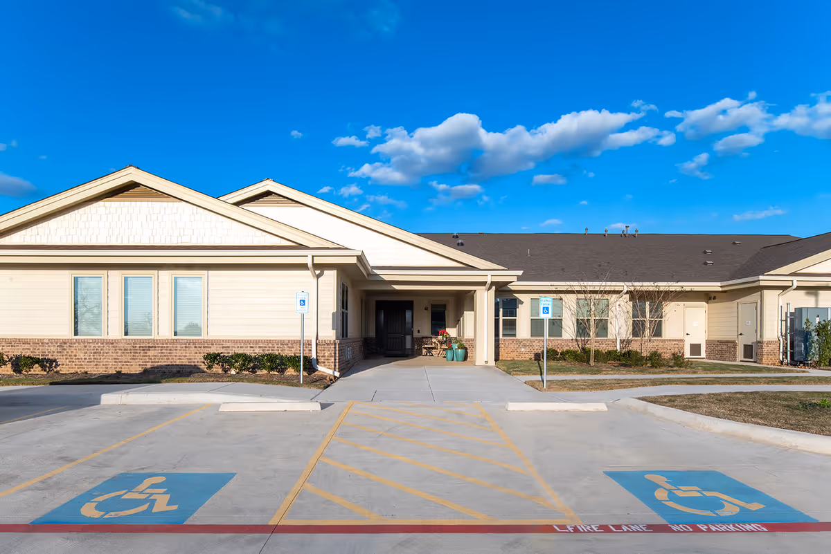 Front exterior of a single-story assisted living facility with a covered entrance, handicap parking spaces, and a clear blue sky.