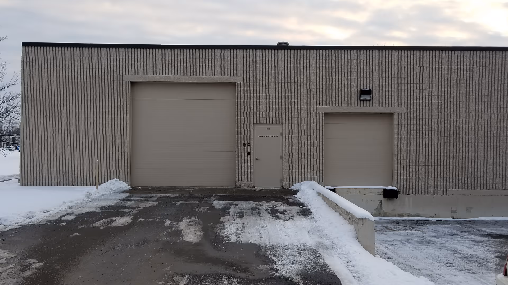 Exterior view of Coram Healthcare facility with two large garage doors and snowy ground.