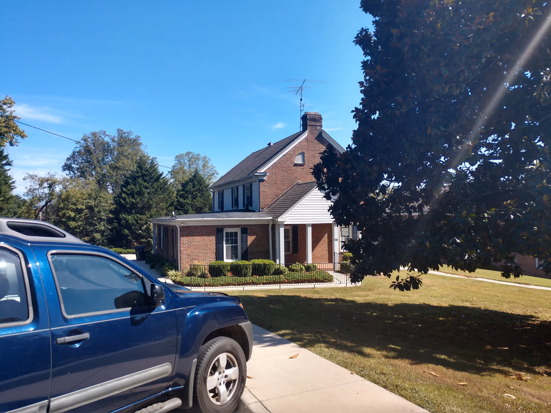 Blue pickup truck in driveway beside a brick house with trees.