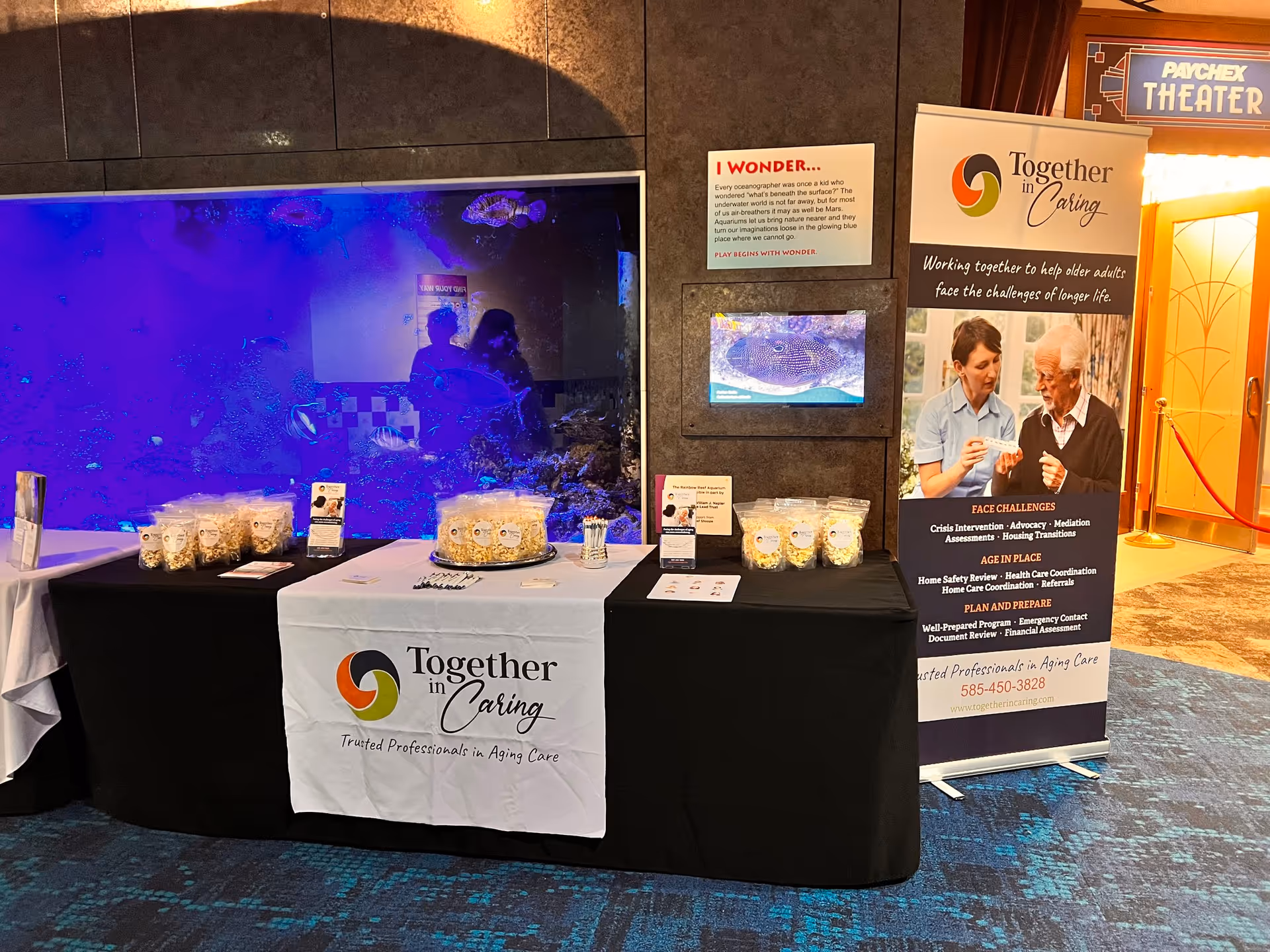 An indoor exhibition table with Together in Caring banners and display materials at an event.