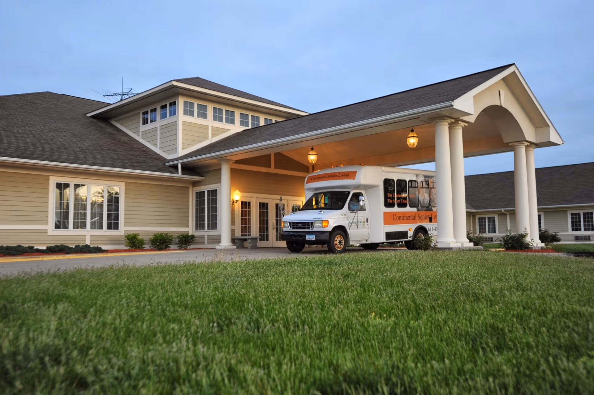 Exterior view of a senior living facility with a shuttle bus under a porte-cochere.