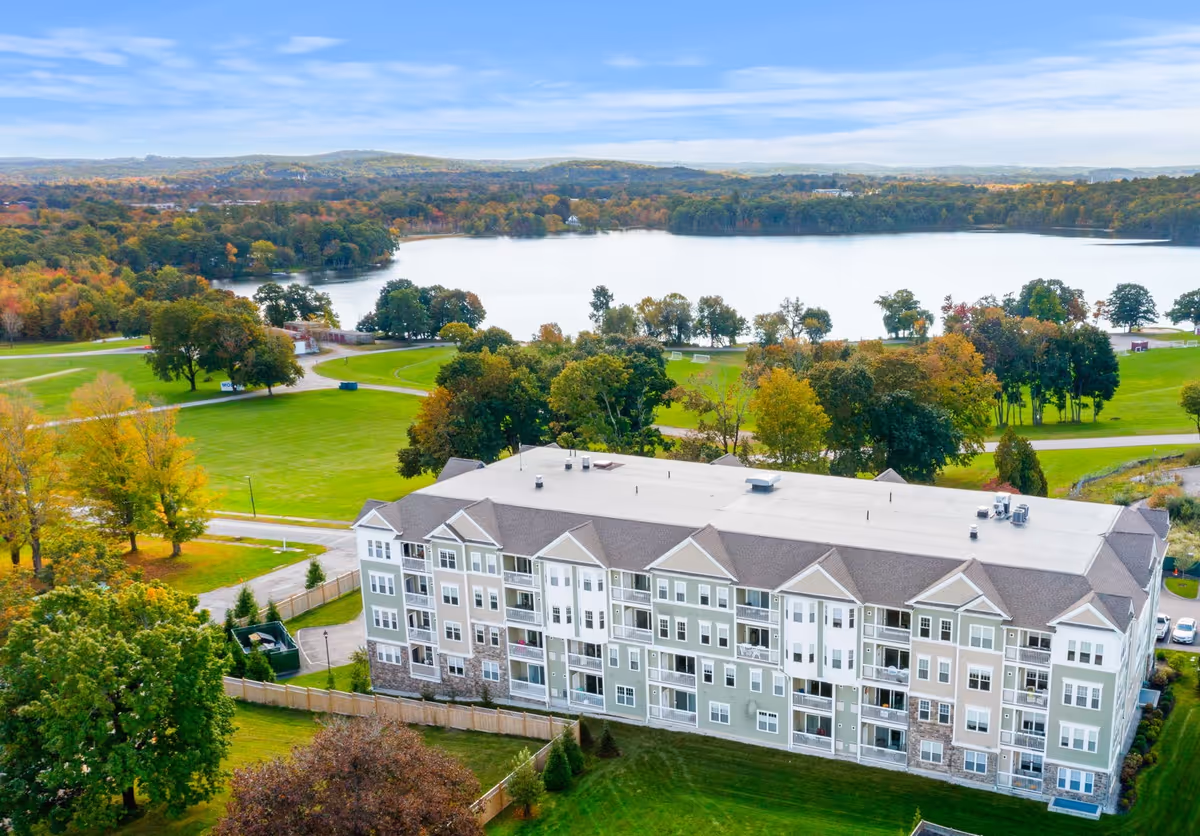 Aerial view of a multi-story senior living building with lake and green grounds