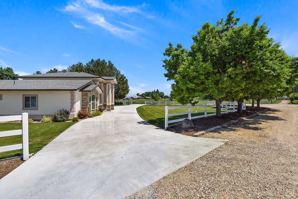Front view of a single-story senior living home with a curved driveway, white fence, and trees.